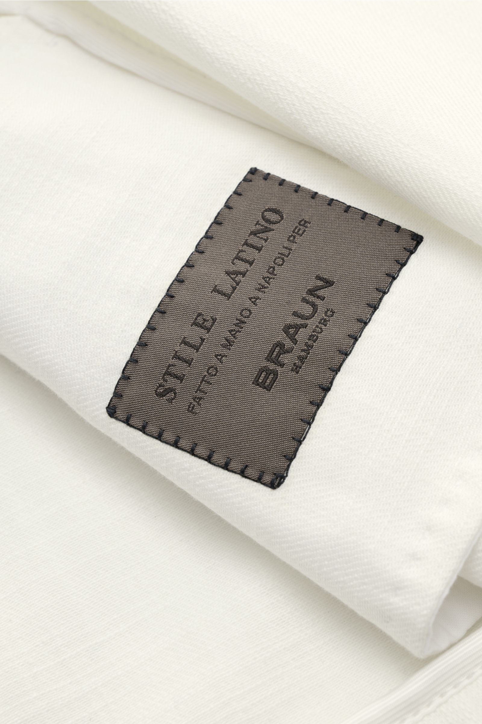 Close-up front angle of the Stile Latino Overshirt 'Gbu Teseo' cream showing the black stitched label on soft pure cotton fabric. Luxurious layers: This sophisticated overshirt by STILE LATINO combines exquisite quality with timeless elegance – a styli