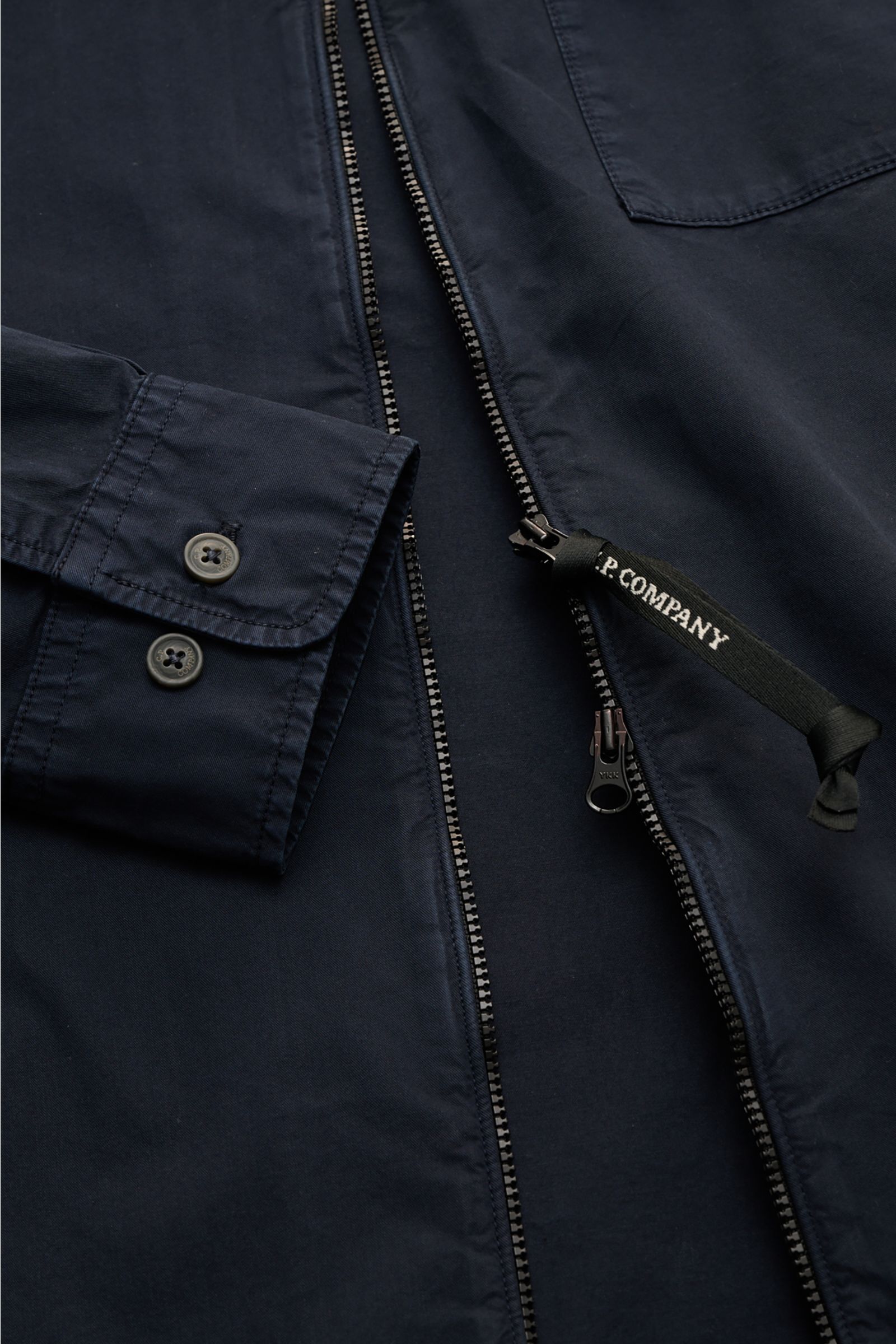 Close-up front view of C.P. Company Overshirt navy showing slim fit, two-way zipper with logo pull, cuff with buttons, chest pocket with flap, and sleeve logo detail.