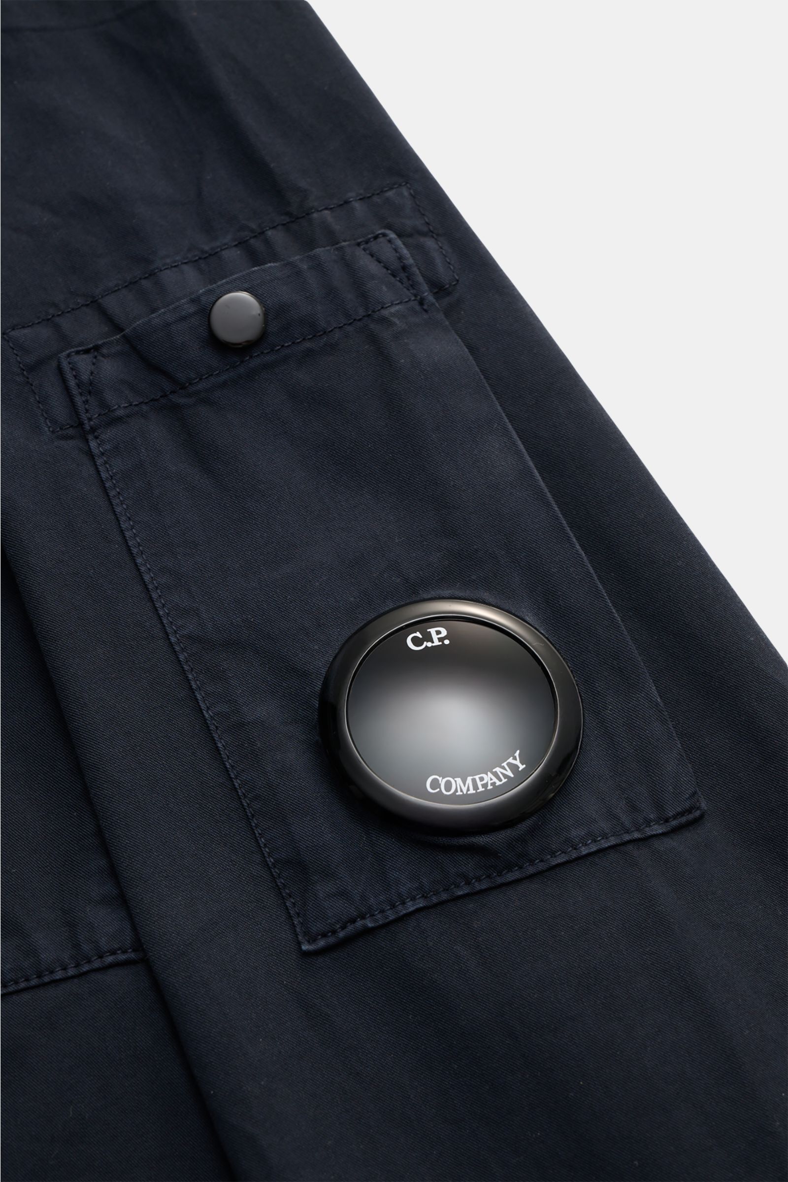 Close-up photo of the C.P. Company Overshirt navy sleeve, showing the chest pocket with flap, button, and round logo detail, made of pure cotton.