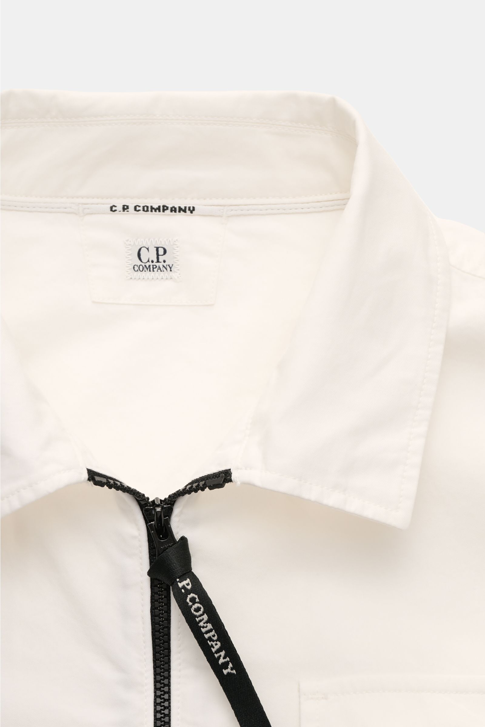Close-up front view of the C.P. Company Overshirt offwhite showing the folded collar, two-way black zipper with logo pull, and chest pocket with flap.