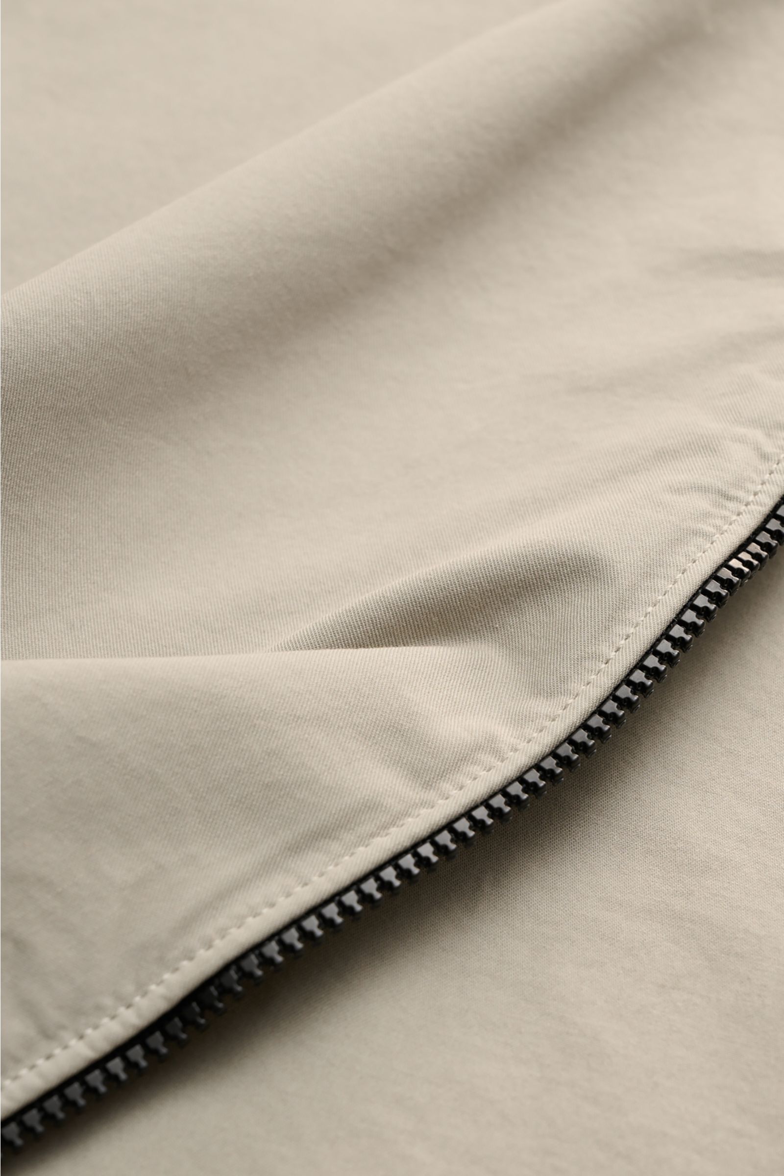 Close-up front view of the C.P. Company Overshirt sand showing the two-way zipper and smooth sand-colored pure cotton fabric, a lightweight slim fit layering piece with a turn-down collar, chest pocket with flap, logo detail pocket on the sleeve, and cuff