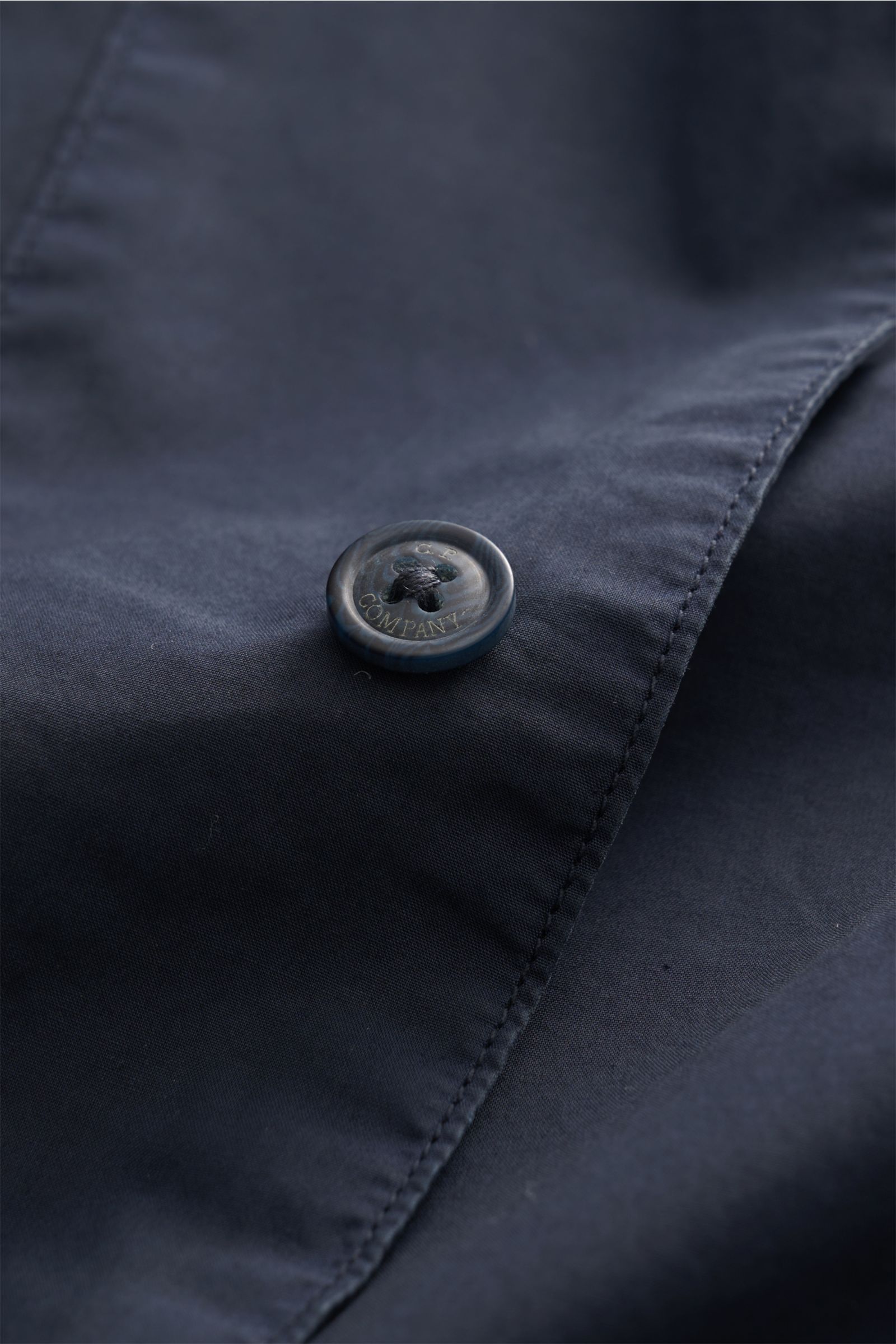 Nahaufnahme eines Knopfs mit C.P. Company Schriftzug auf dem navy C.P. Company Overshirt navy aus reiner Baumwolle, Slim Fit, leichte Qualität.