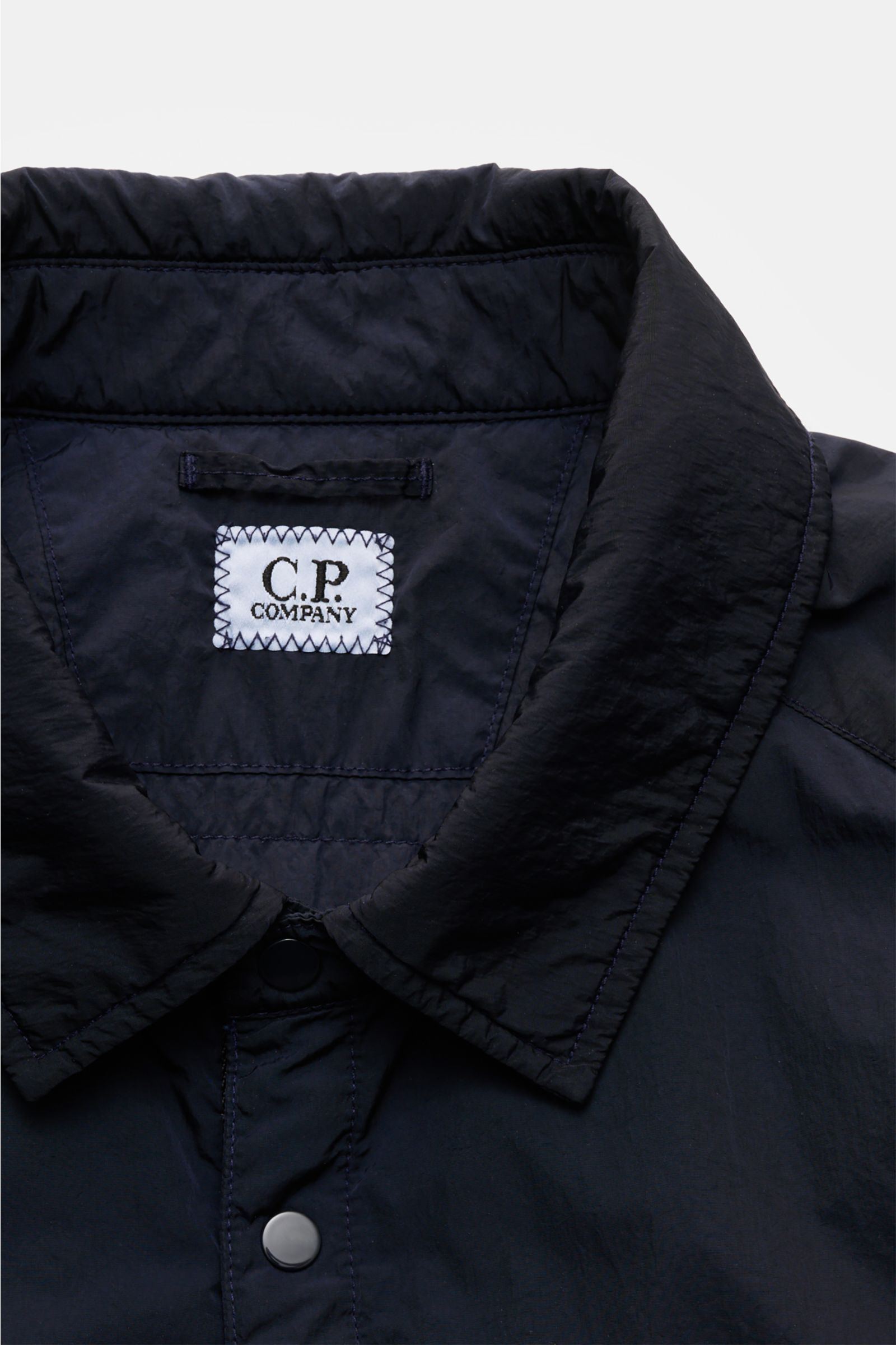 Close-up front view of C.P. Company Overshirt dark navy showing turn-down collar, snap button placket, and fabric texture, perfect for changeable spring weather with high-quality microfibre, slim fit, patch breast pocket, side seam pockets, cuffs with but