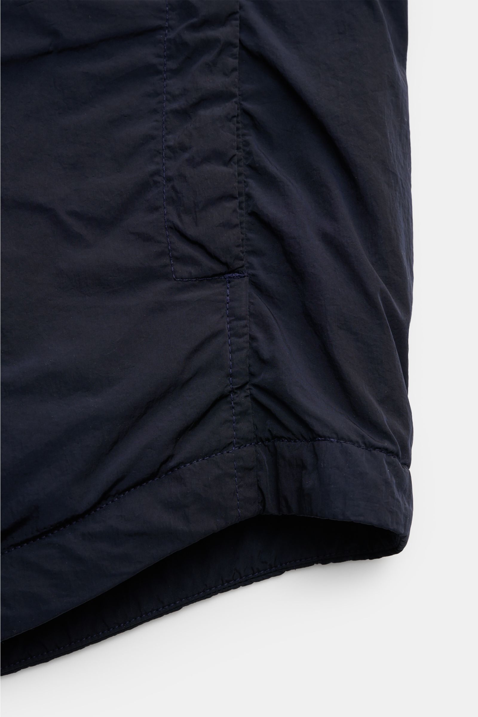 Close-up side view of the slightly rounded hem of the C.P. Company Overshirt dark navy, made of high-quality microfibre, slim fit, snap button placket, turn-down collar, patch breast pocket, side seam pockets, cuffs with buttons, upper sleeve pocket, sign