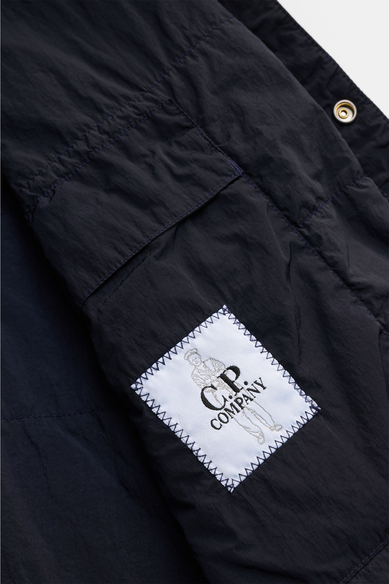 Close-up side view of C.P. Company Overshirt dark navy showcasing the patch breast pocket, snap button placket, and signature lens detail, made of high-quality microfibre, slim fit, with turn-down collar, cuffs with buttons, pockets in side seam, pocket o