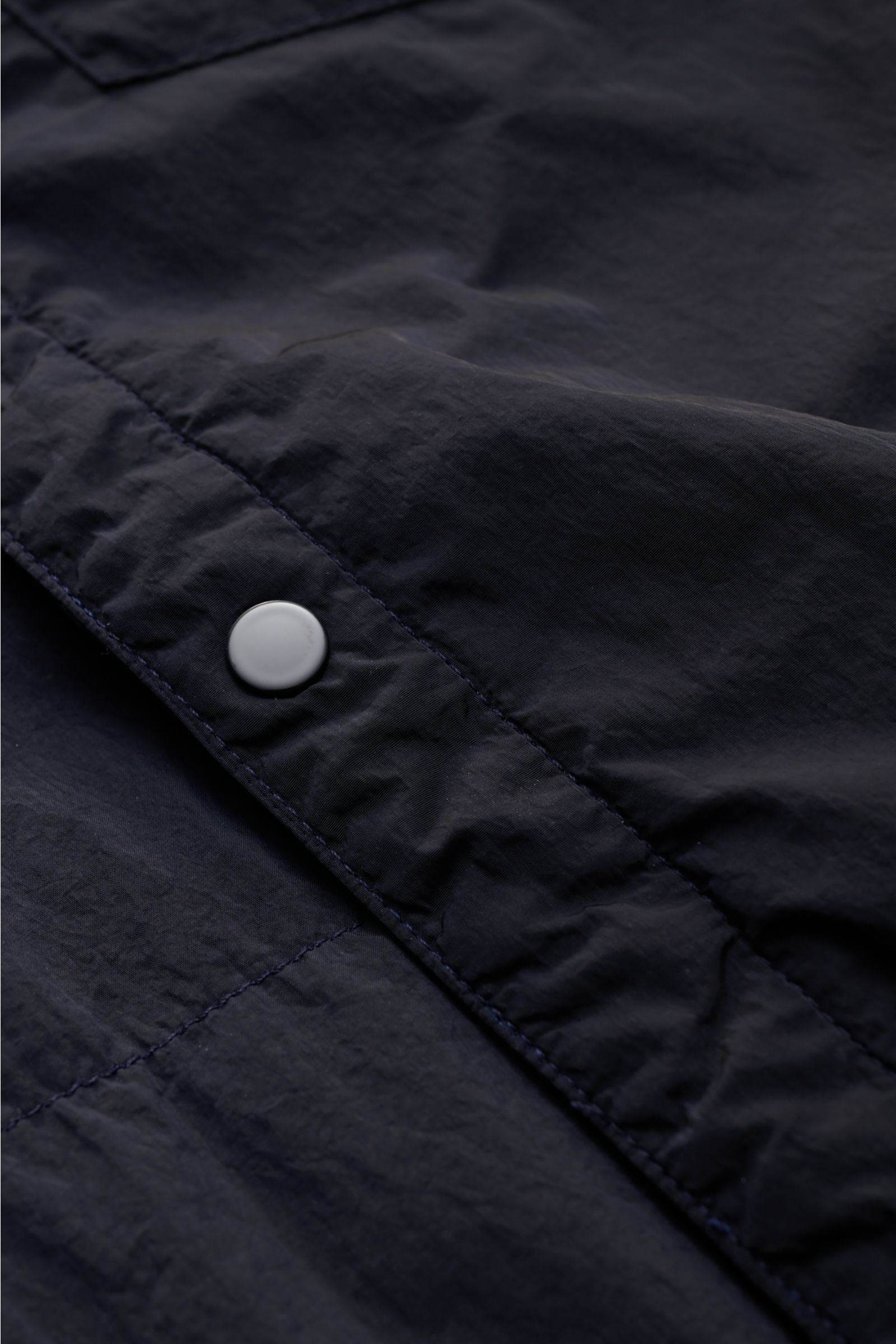 Close-up view of a snap button on the C.P. Company Overshirt dark navy made of high-quality microfibre, slightly robust to the touch, perfect for changeable spring weather.