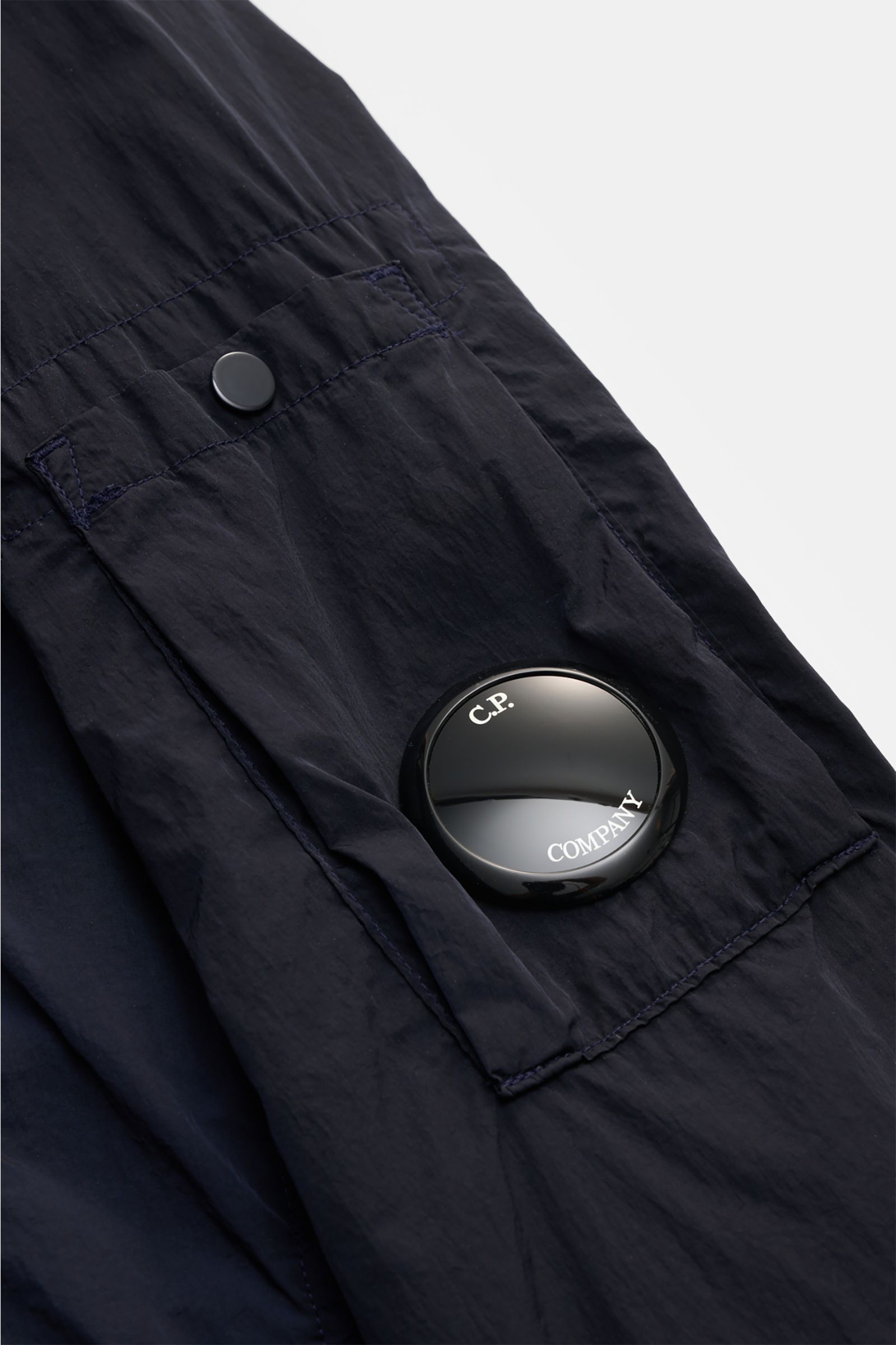 Close-up perspective of the upper sleeve pocket on the C.P. Company Overshirt dark navy, showing the signature lens detail and snap button. Perfect for changeable spring weather, this overshirt features high-quality microfibre, a slightly robust touch, sl