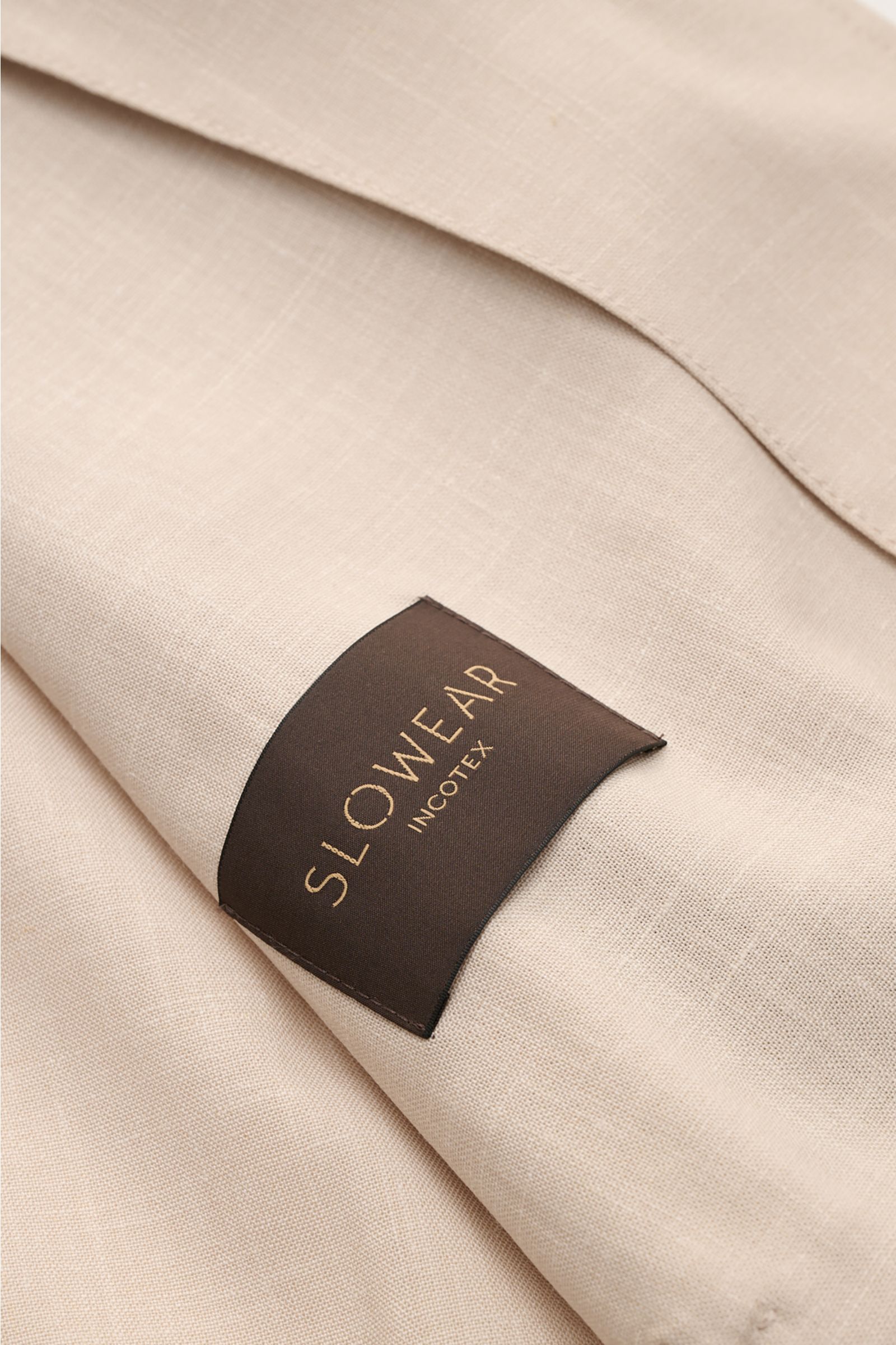 Close-up, angled view of the Incotex Overshirt beige mottled showing fabric texture and black 'SLOWEAR INCOTEX' label, made of luxurious virgin wool-silk blend with six-button placket, turn-down collar, jetted front pockets, button cuffs, elasticated hem,