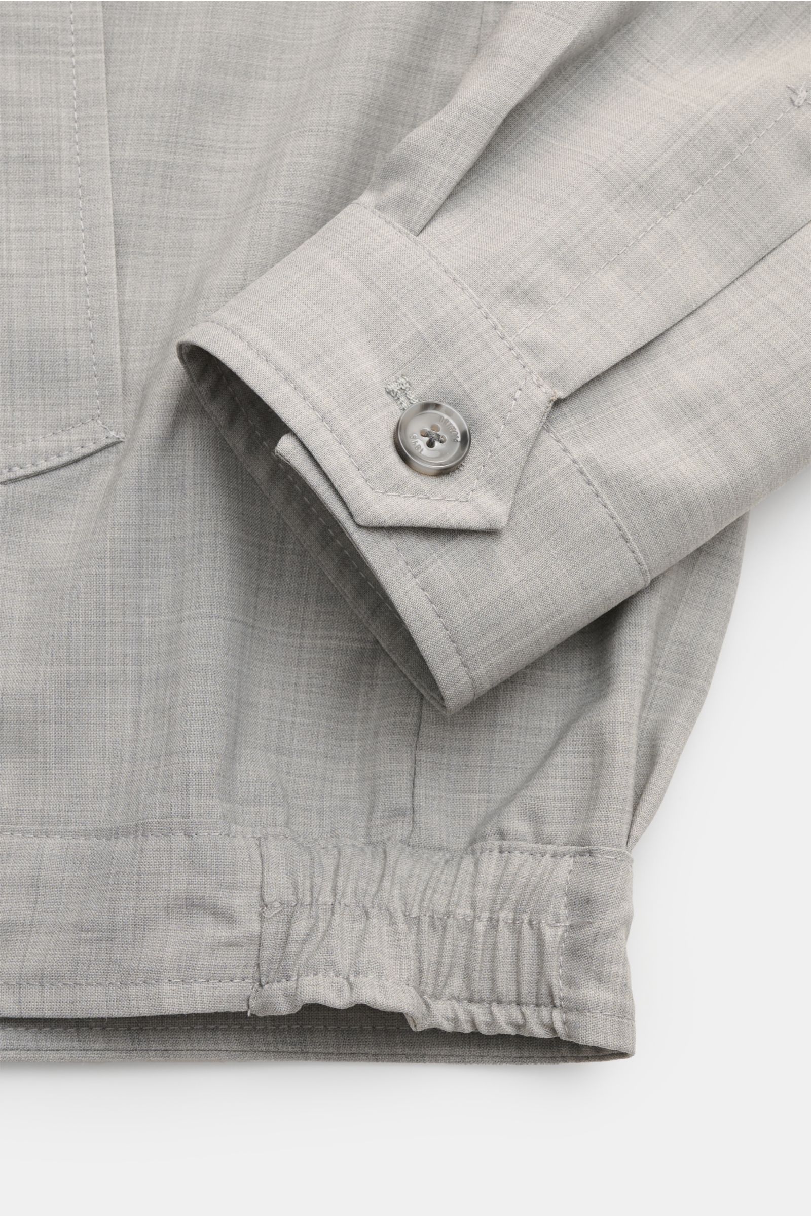 Close-up from a top-front perspective of the Briglia 1949 Overshirt 'Bill' grau meliert showing the sleeve cuff with button and elastic hem in a melierte wool-microfiber mix fabric.

Italienisches Flair in Ihrer Garderobe erhalten Sie mit dem smarten O