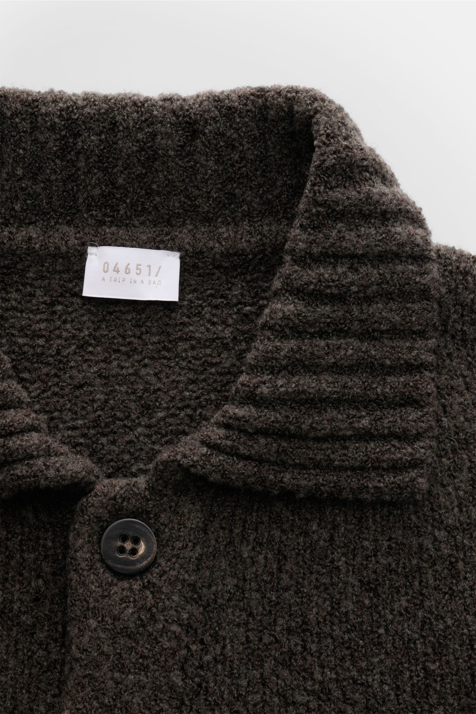 04651/ A trip in a bag Cardigan 'Grainy' dunkelbraun aus wärmendem Woll-Mix, Boucléstrick, Slim Fit, Umlegekragen, Brusttasche, Sechs-Knopf-Leiste, breiten Rippbündchen, Detailansicht von oben.