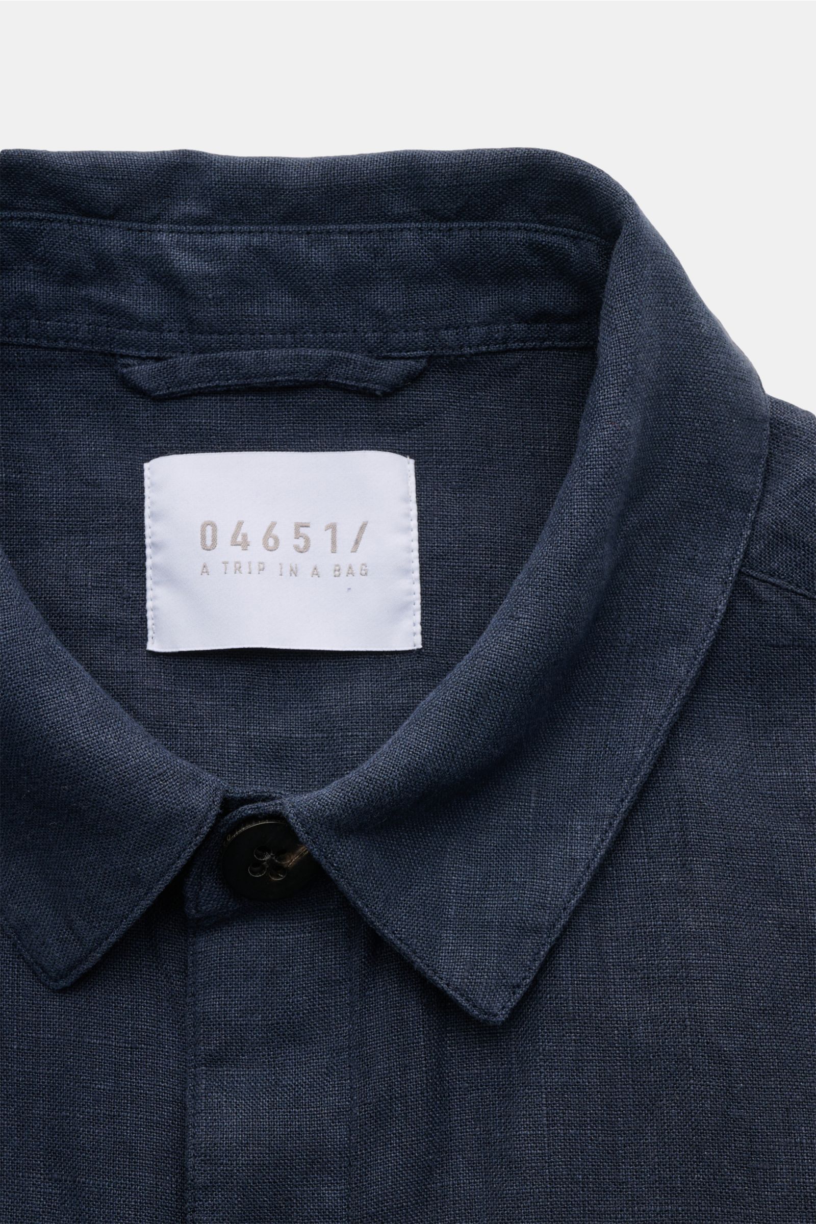 Nahaufnahme aus frontaler Perspektive des Kragens und des weißen Markenlabels des 04651/ A trip in a bag Overshirt 'Linen Jacket' navy aus weichem, reinem Leinen mit Slim Fit.