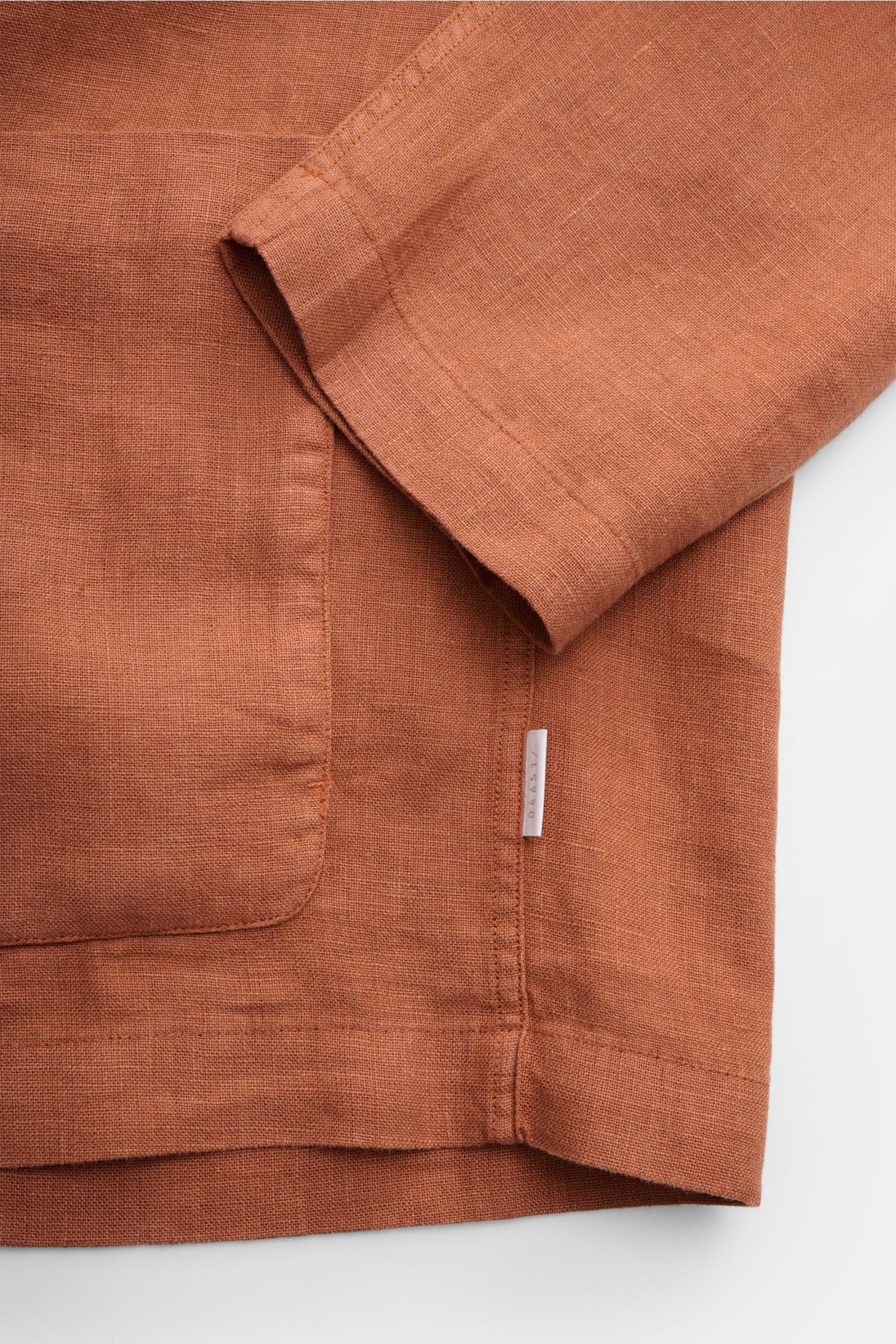 Nahaufnahme des Ärmels und der aufgesetzten Fronttasche des 04651/ A trip in a bag Overshirt 'Linen Jacket' rostbraun aus reinem Leinen mit weichem Griff, fotografiert von schräger Oberseite.