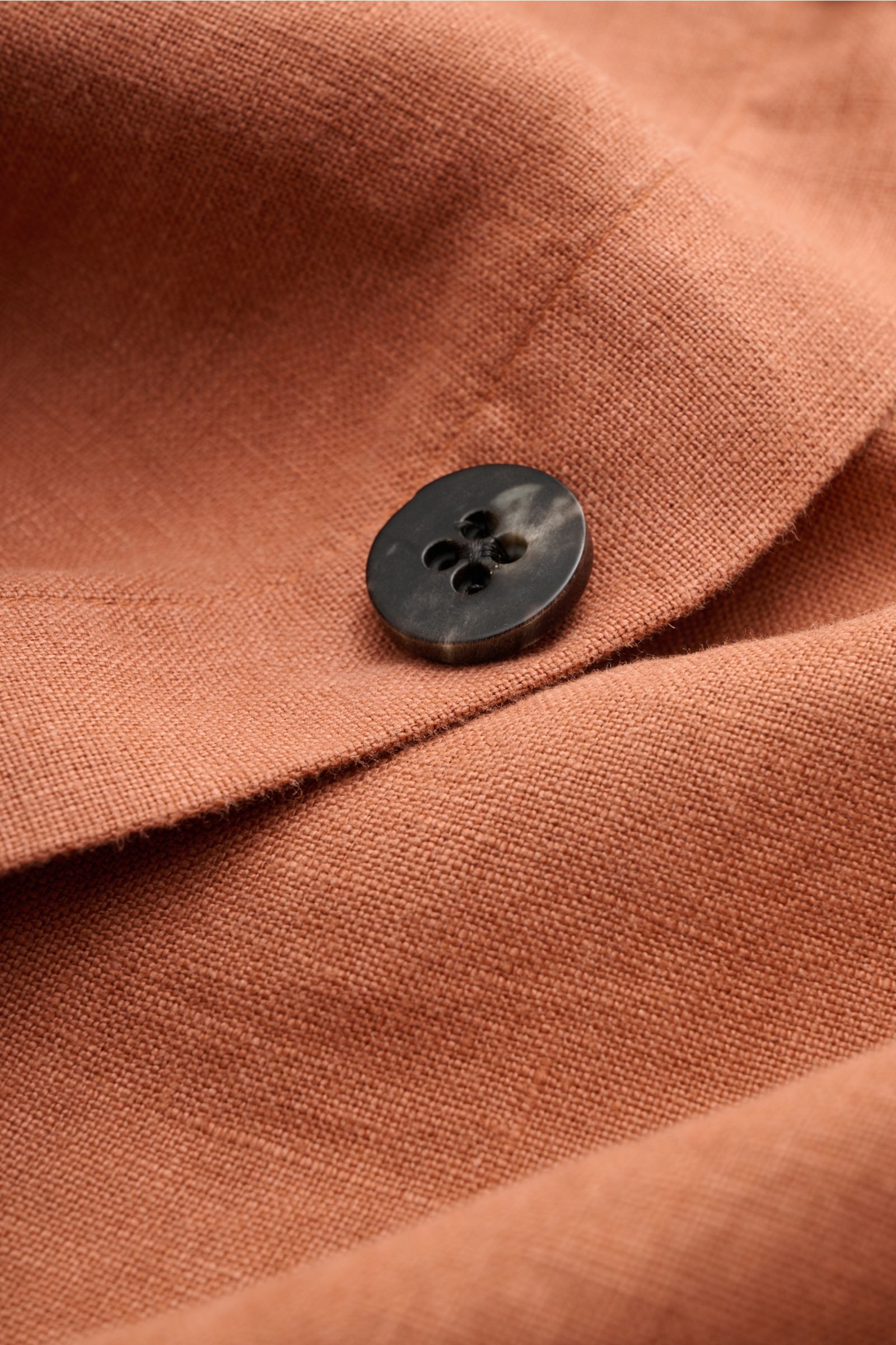 Nahaufnahme eines schwarzen Knopfes auf dem rostbraunen reinen Leinenstoff des 04651/ A trip in a bag Overshirts 'Linen Jacket' mit weichem Griff, Slim Fit und feiner Struktur.