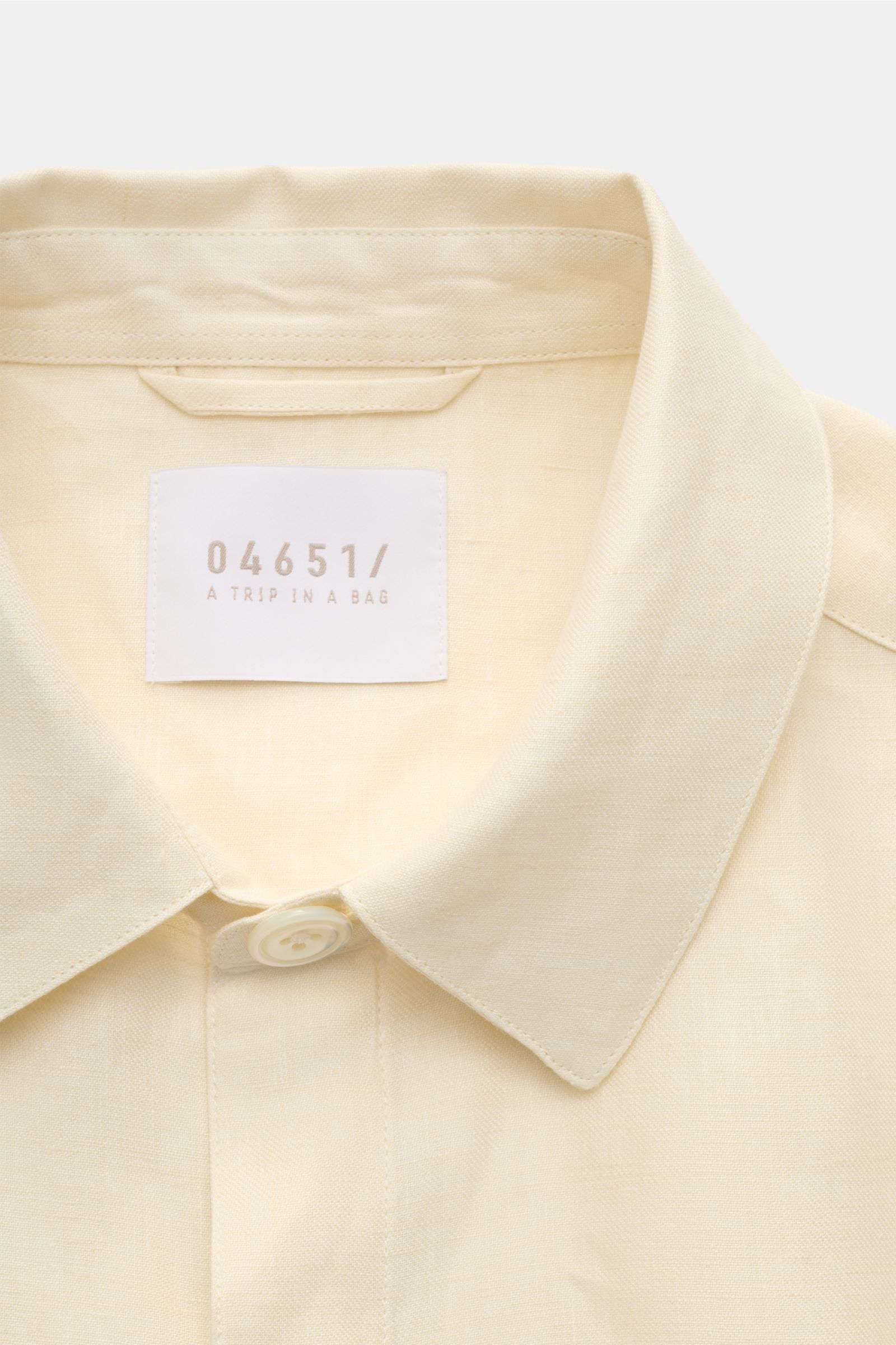 Close-up front view of the collar and label of the 04651/ A trip in a bag Overshirt 'Linen Jacket' cream, made from pure linen with a soft feel and slim fit. For casual linen looks: This overshirt by 04651/ A TRIP IN A BAG is made of summery linen fabric 