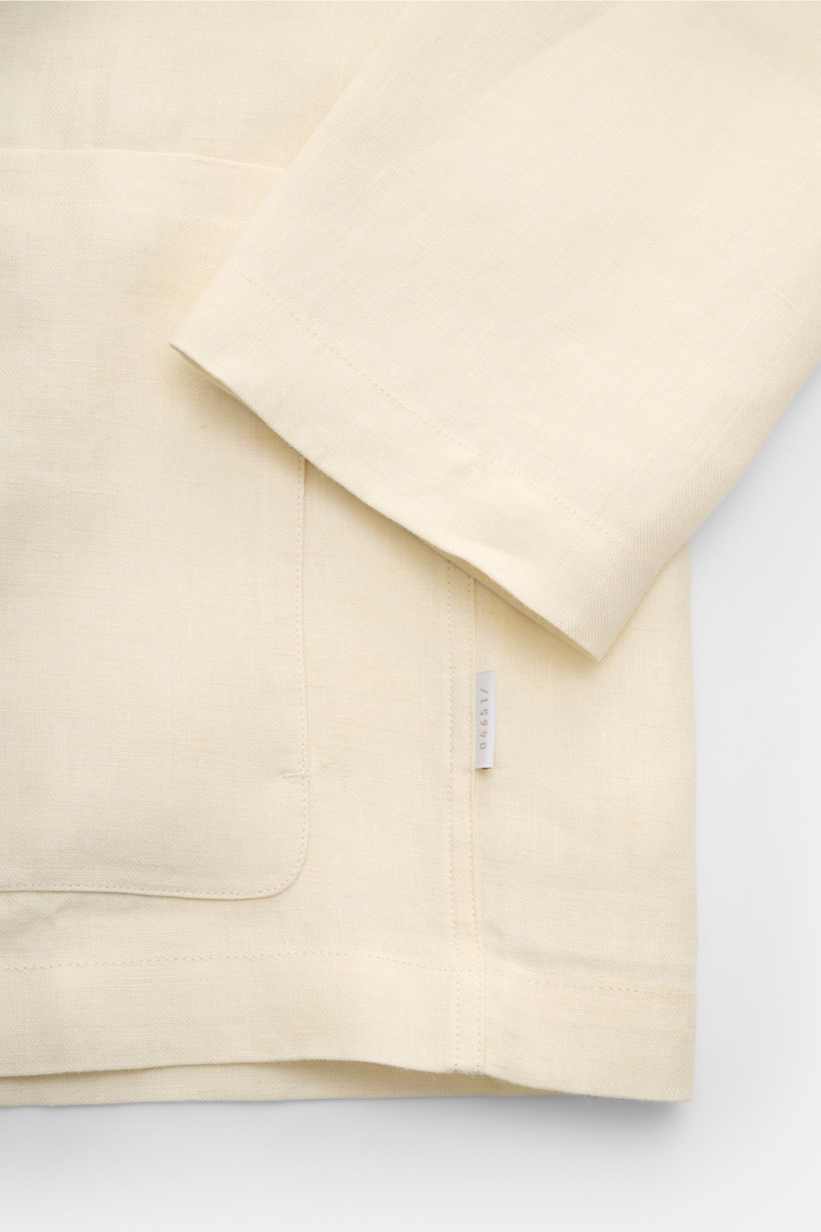 Nahaufnahme des cremefarbenen 04651/ A trip in a bag Overshirt 'Linen Jacket' aus reinem Leinen, Slim Fit, mit aufgesetzter Fronttasche und weichem Griff, fotografiert von vorne unten.