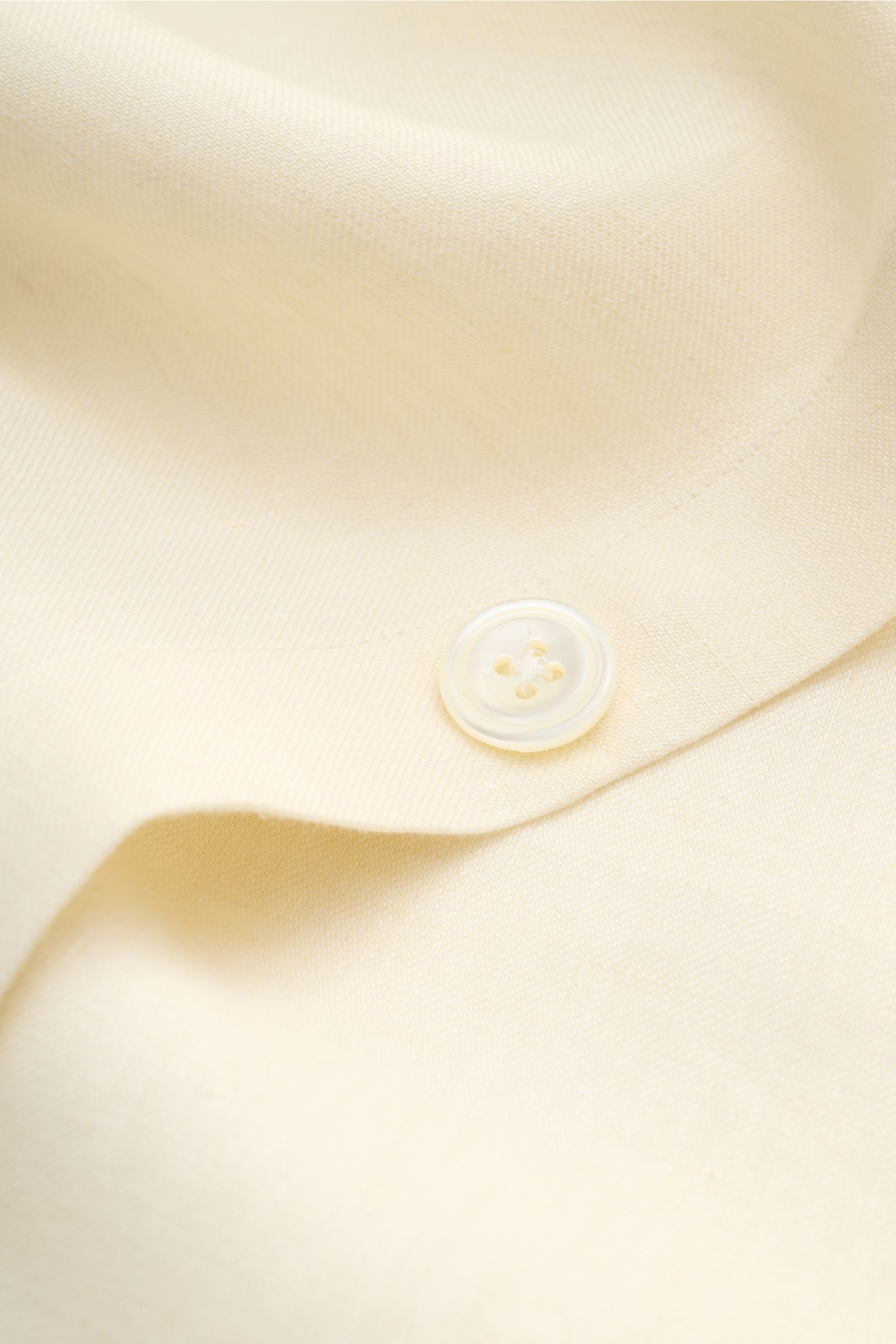 Nahaufnahme des cremefarbenen 04651/ A trip in a bag Overshirt 'Linen Jacket' aus reinem Leinen mit Knopf und weichem Griff, Detailansicht.