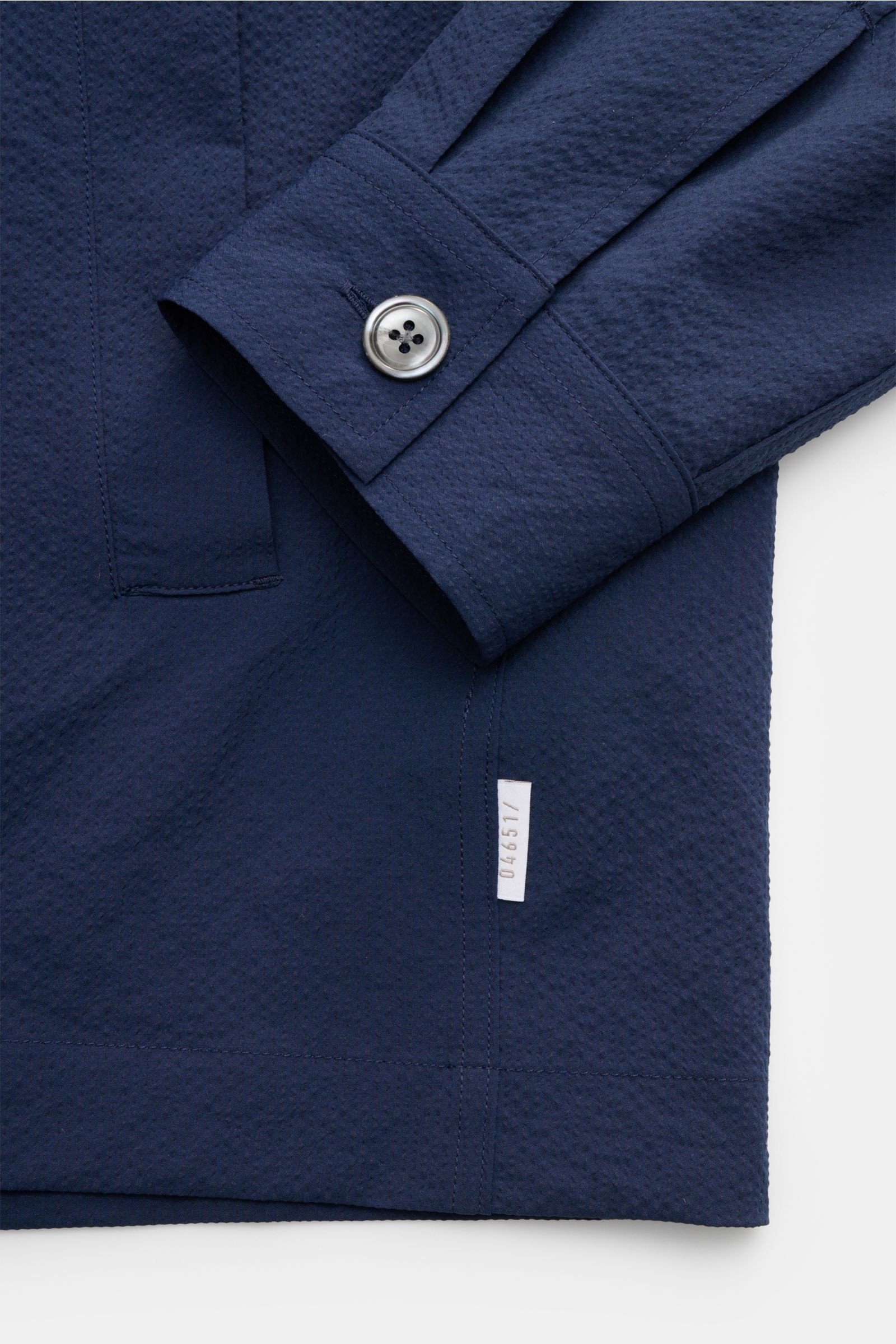 Nahaufnahme des Ärmels und unteren Bereichs des 04651/ A trip in a bag Overshirt 'Technical Seersucker' navy aus strukturierter Microfaser, Slim Fit, mit Fünf-Knopf-Leiste, Umlegekragen und paspelierten Fronttaschen, fotografiert von schräg oben.