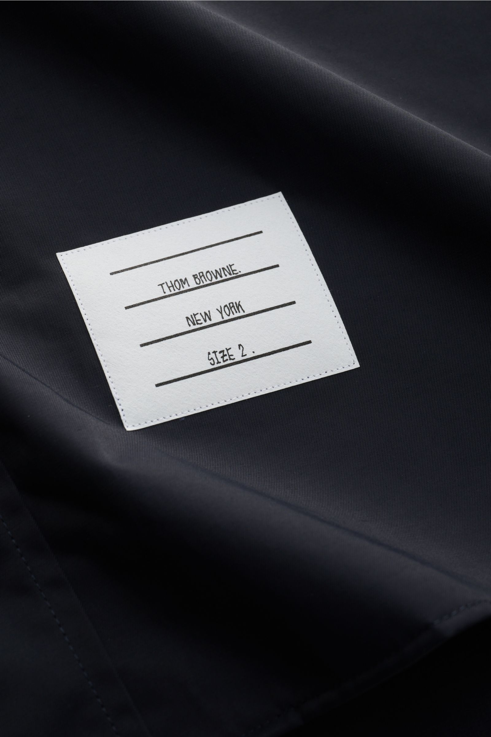 Close-up of the Thom Browne Overshirt - F1066 fabric and label, photographed from above showing smooth black cotton-microfiber blend.

Description: Luxuriöses Layering-Piece: Das Overshirt von THOM BROWNE überzeugt mit seinem sportiv-funktionalen Desig