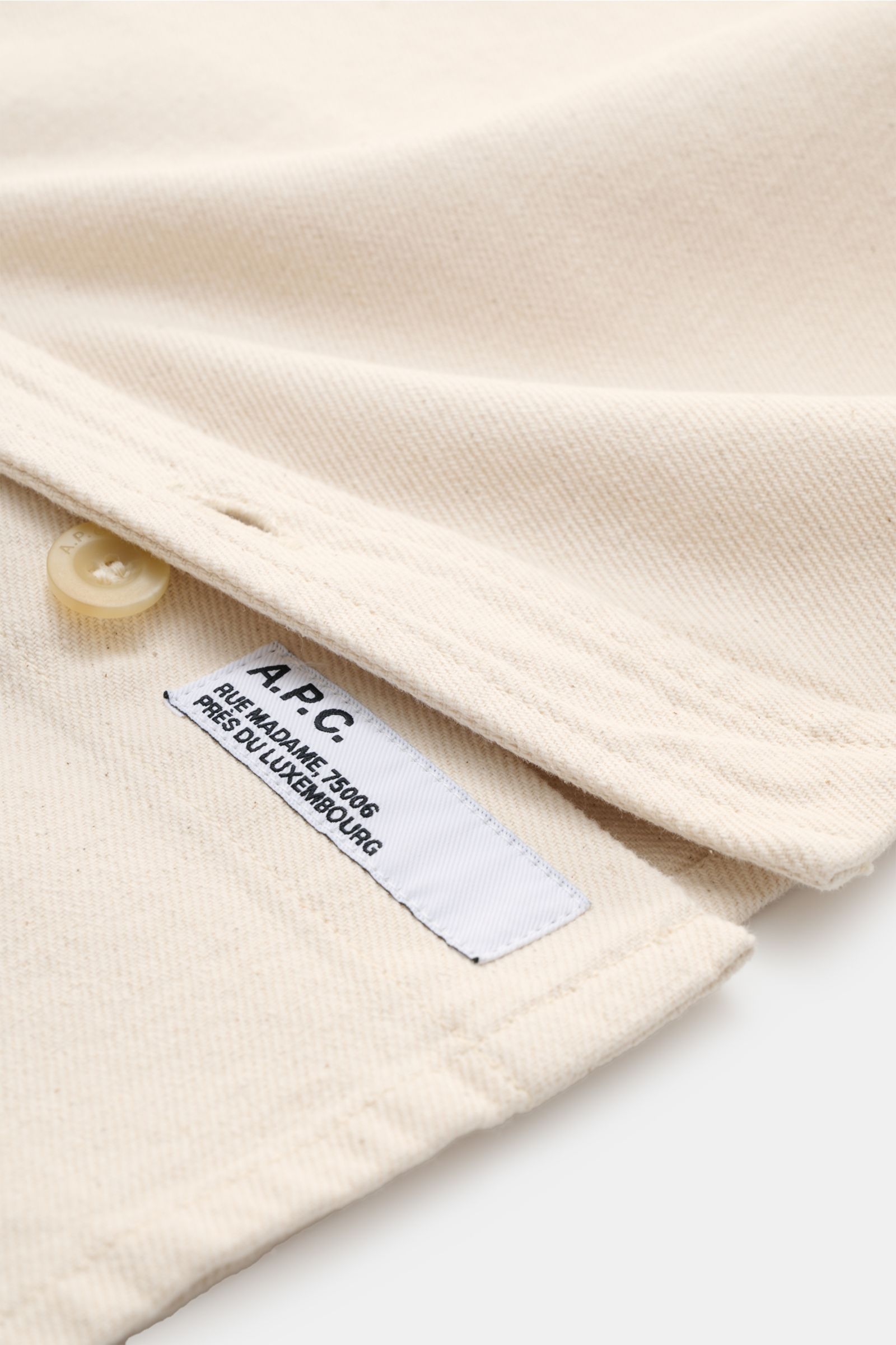 Nahaufnahme von A.P.C. Overshirt sand meliert, Baumwoll-Denim, robust, garment dyed, Regular Fit, Knopf, Label, Detailansicht Kragen und Brusttasche.