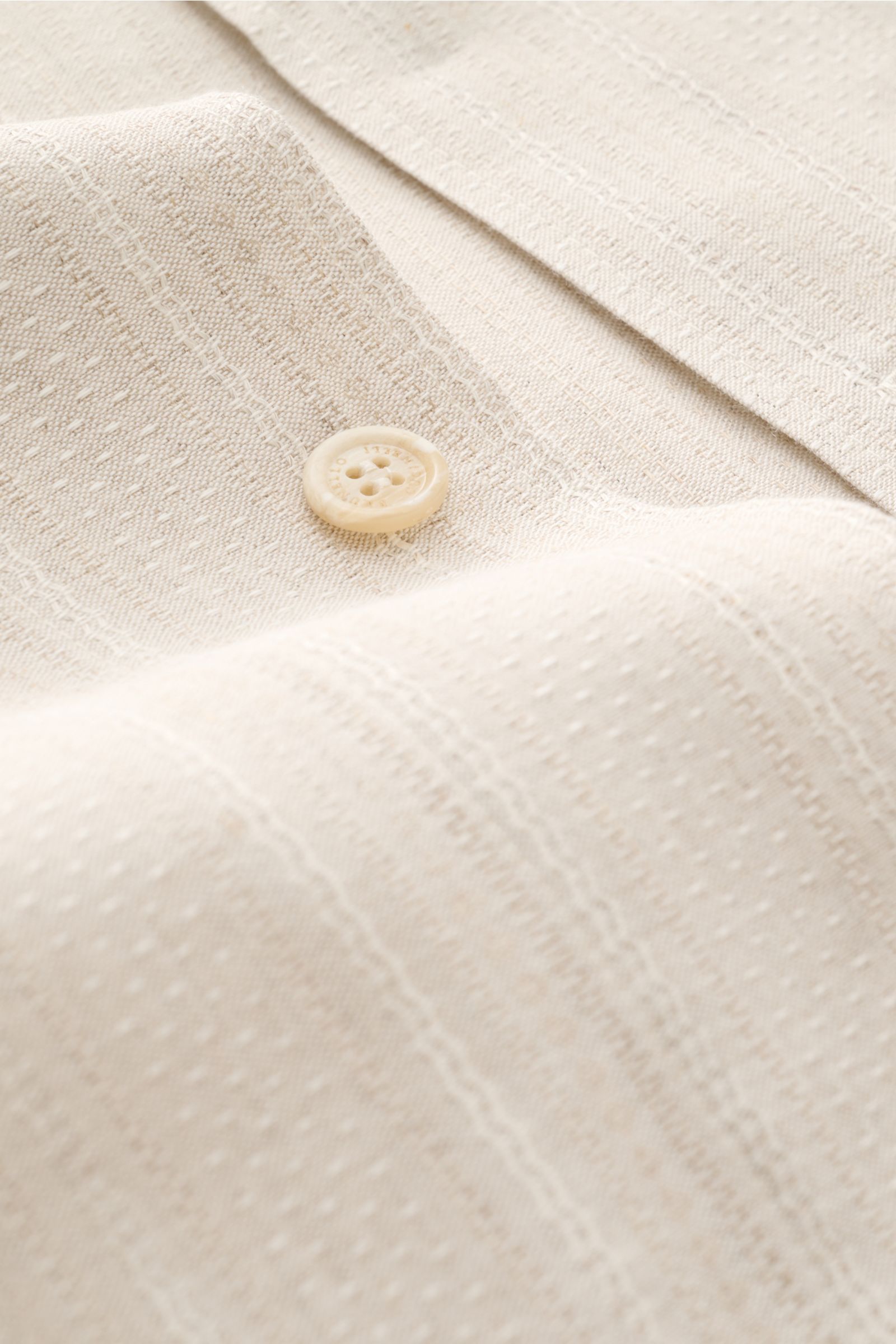 Close-up front view of the beige Brunello Cucinelli Overshirt fabric and button, showing linen-cotton mix texture with seven-button placket and unconstructed design.