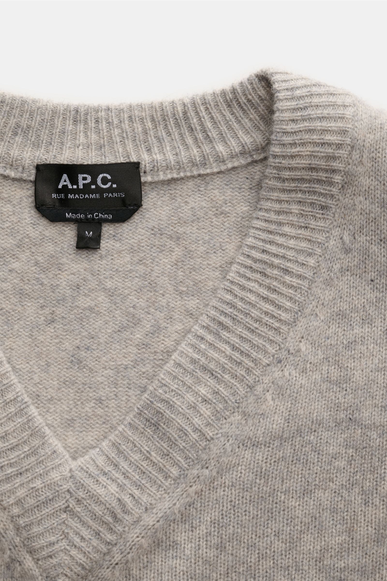 Close-up top-down view of the A.P.C. V-Neck Pullover 'Pull Dany' grau meliert showing the V-neck collar and label, made from reine Yak-Wolle, with weicher Griff, mittelfeines Strickbild, Slim Fit, and flexible Rippbündchen.