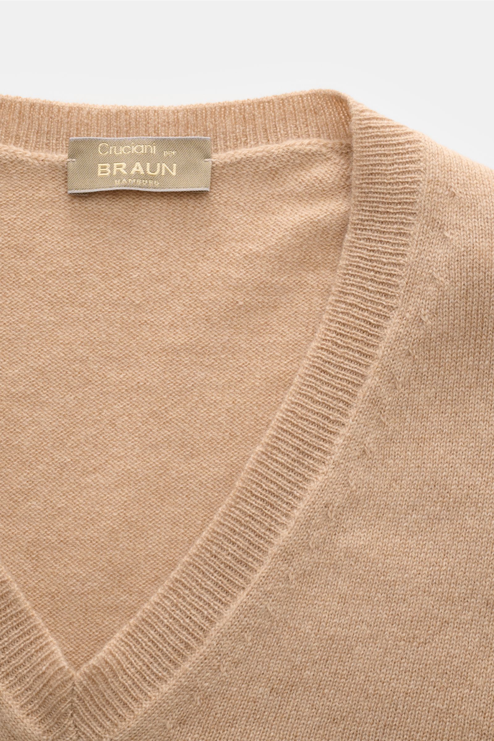Close-up top-down view of Cruciani Cashmere V-neck jumper beige showing fine knit, slim fit, smooth touch, ribbed bands, and label.

This V-neck jumper in pure cashmere by CRUCIANI is the epitome of understatement and style. Its smooth feel and fine kn