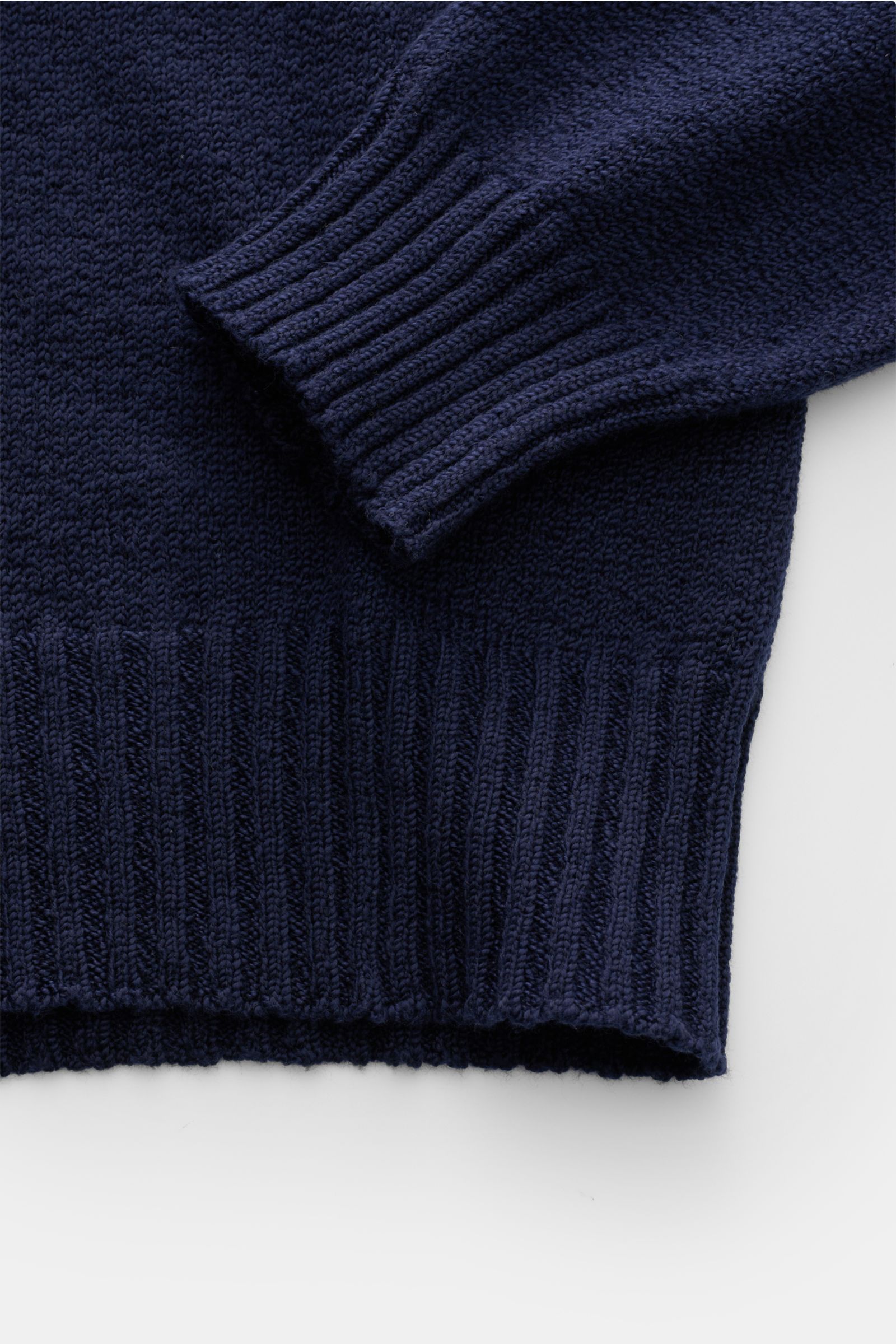 Nahaufnahme des dunkelblauen Drumohr V-Neck Pullovers aus reiner Baumwolle mit Bouclé-Struktur, breiten Rippbündchen, Slim Fit, mittelfeinem Strickbild, seitlich fotografiert.