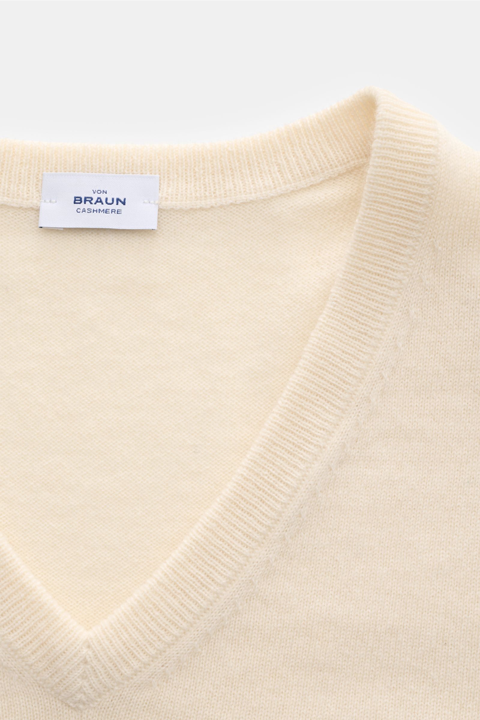 Close-up front view of the von Braun Cashmere V-Neck Pullover creme showing the soft, fine knit and V-neckline with a label inside the collar. 

Geschmeidiges Basic für die kalte Jahreszeit: Der VON BRAUN V-Neck Pullover – gefertigt aus reinem Cashme