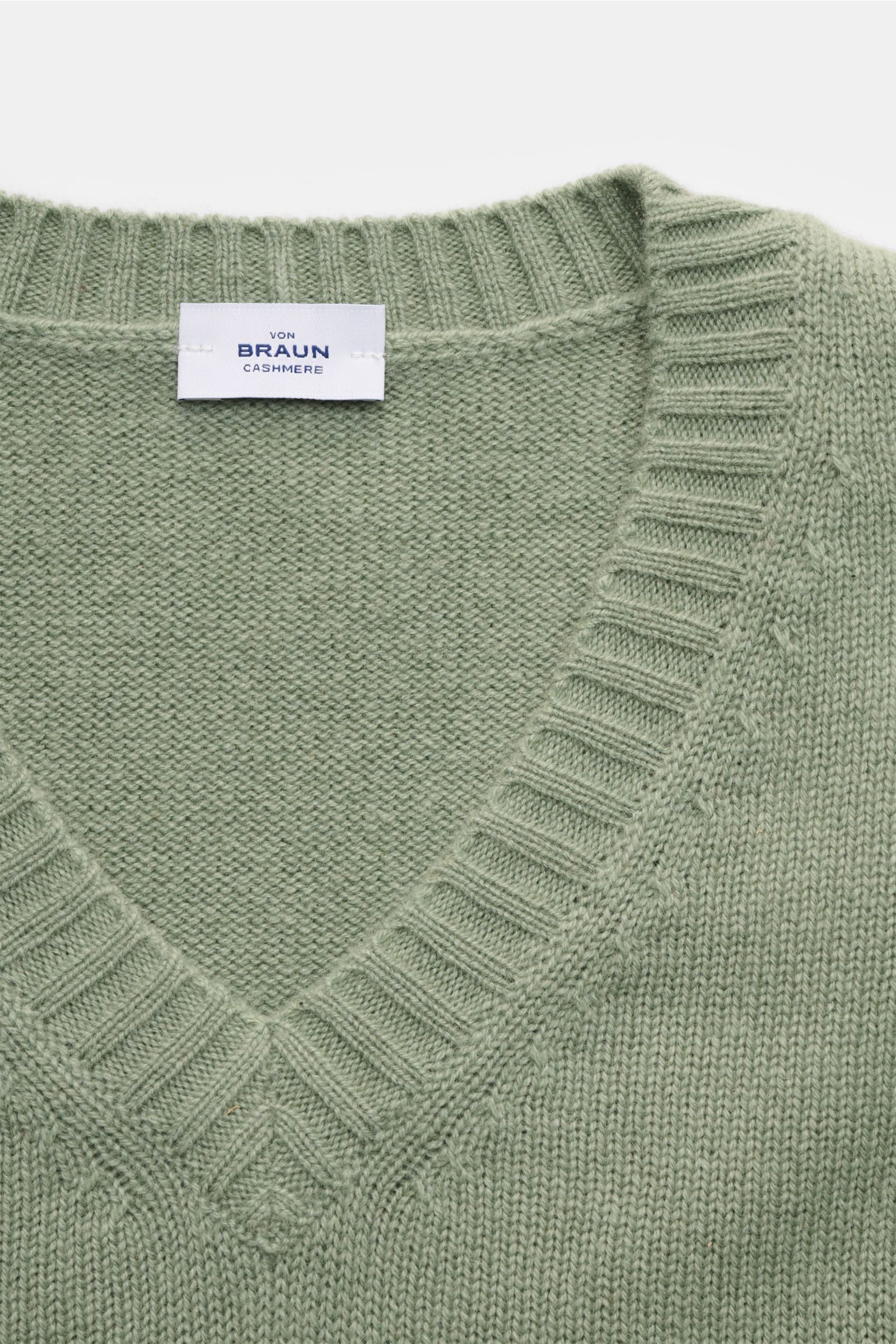 Nahaufnahme von oben auf den von Braun Cashmere V-Neck Pullover salbei mit mittelfeinem Strickbild, V-Ausschnitt und elastischen Rippbündchen.
