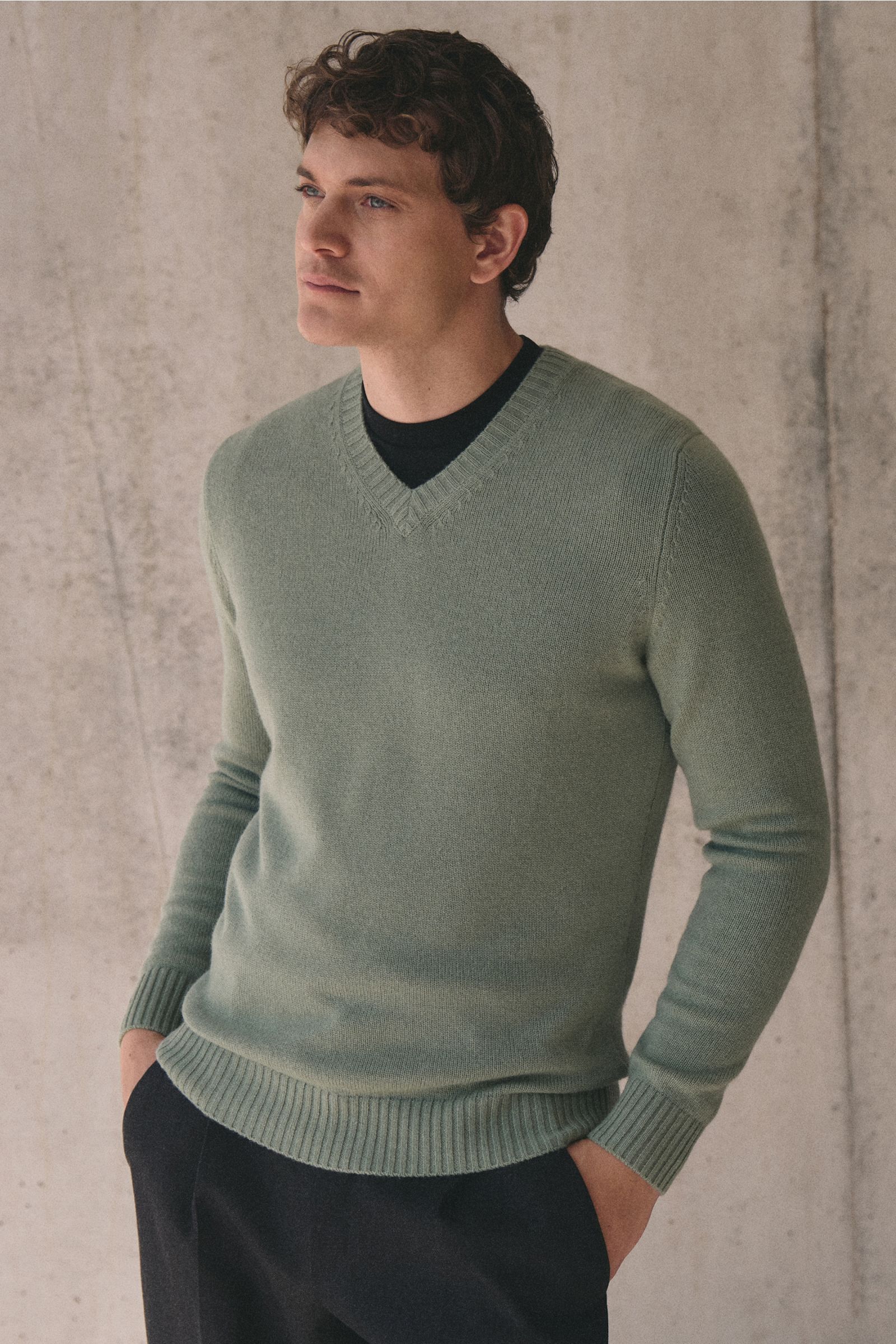 Junger Mann von vorne seitlich fotografiert trägt den von Braun Cashmere V-Neck Pullover salbei mit V-Ausschnitt und elastischen Rippbündchen.