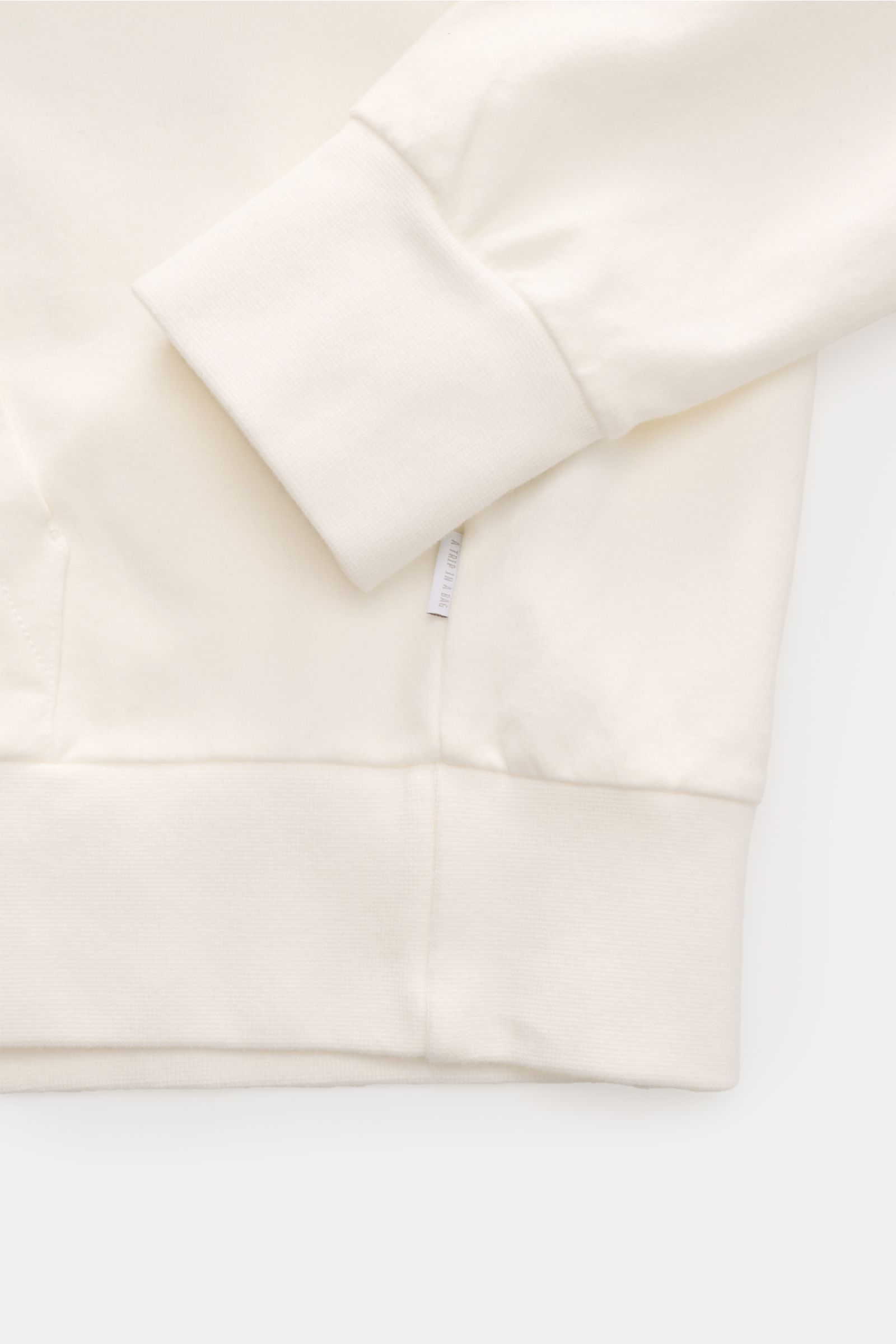 Close-up side view of the cuff and hem of the 04651/ A trip in a bag Kapuzenpullover 'IF Hoodie' offwhite in soft brushed elastic cotton with ribbed edges and a small side label.