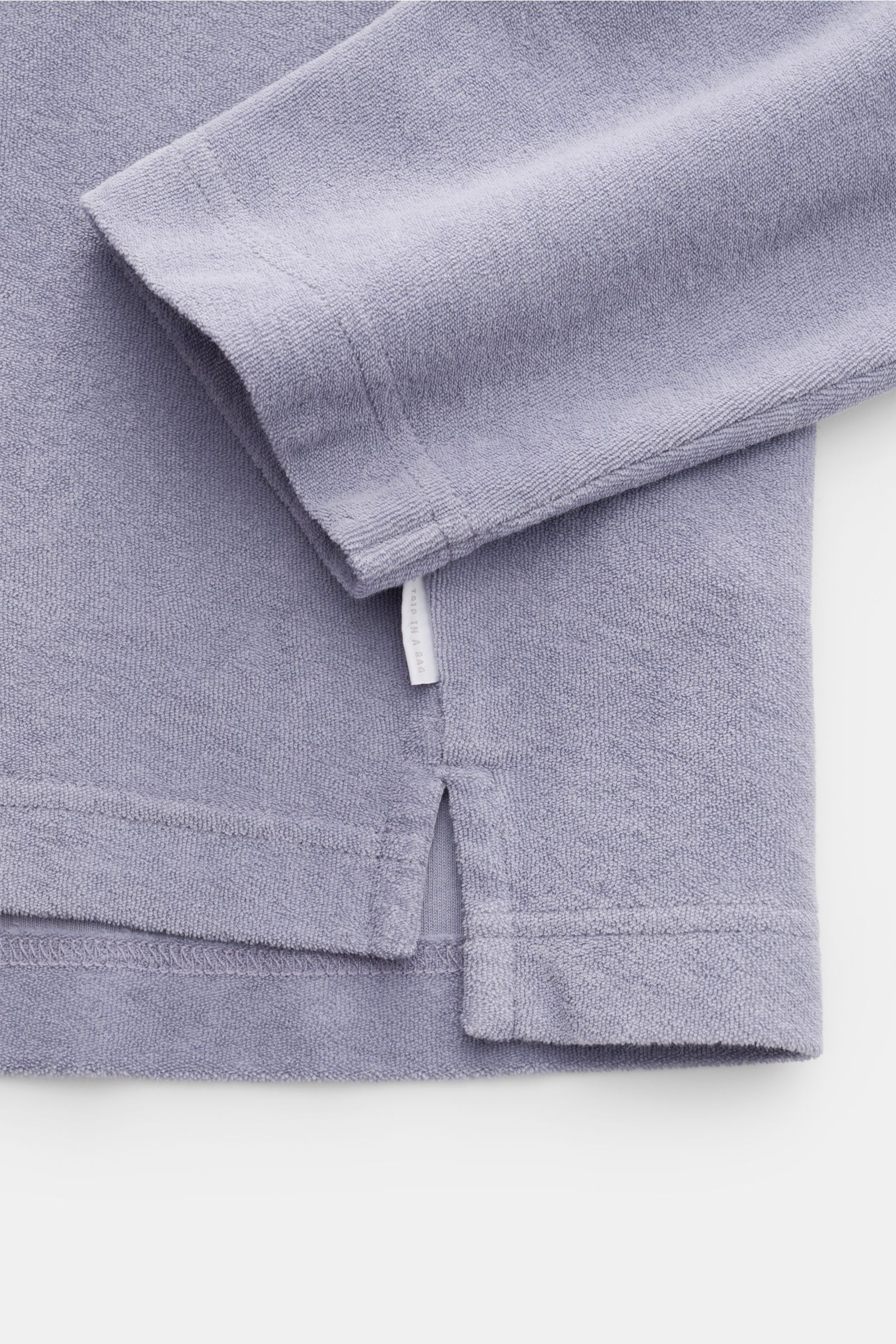 Detailaufnahme des lavenderfarbenen 04651/ A trip in a bag Frottee-Kapuzenpullovers 'Terry' aus reiner Baumwolle mit weichem Griff, Regular Fit, Kapuze und kleinem Weblabel in der Seitennaht, fotografiert von unten schräg seitlich.