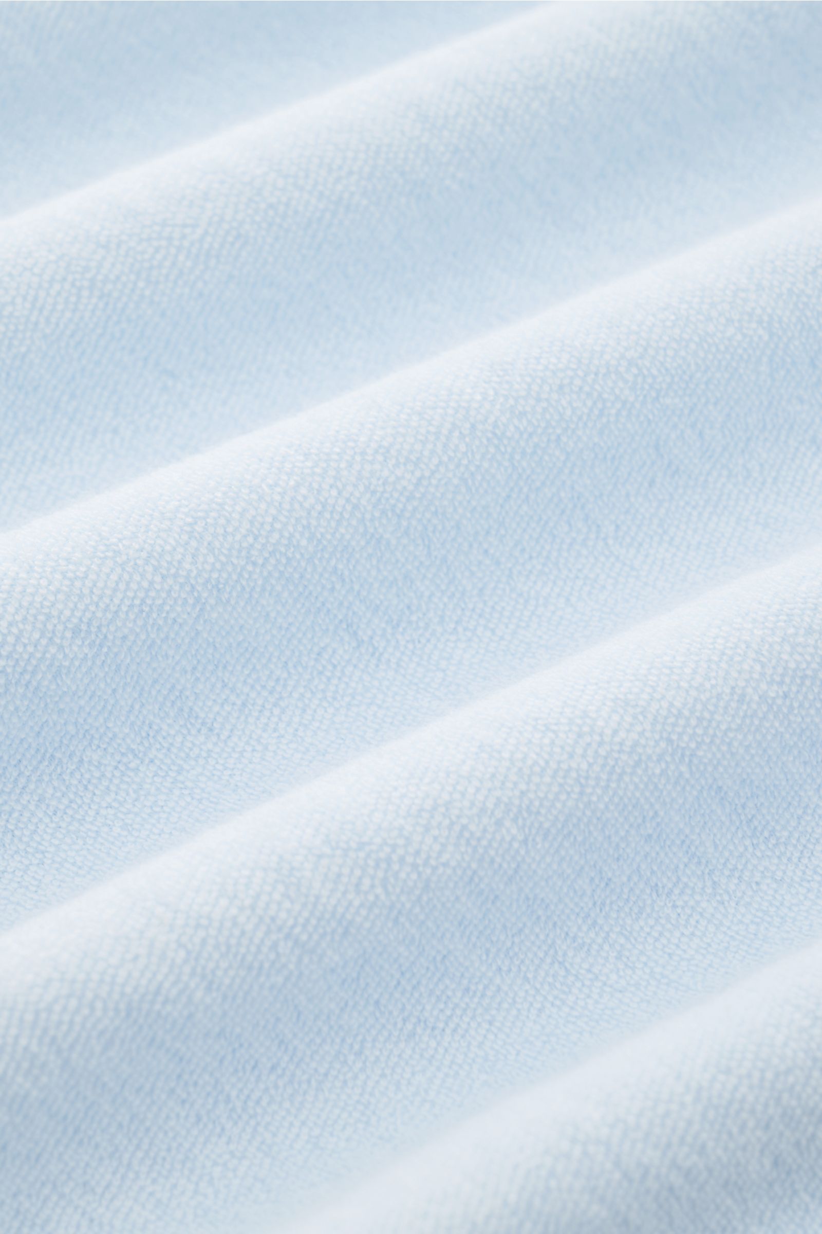 Close-up front view of pastel blue terrycloth fabric of the 04651/ A trip in a bag Terry hooded jumper 'Terry' showing soft texture and gentle folds. Comfort and coolness with summery nonchalance: The hooded jumper 'Terry' by 04651/ A TRIP IN A BAG made o