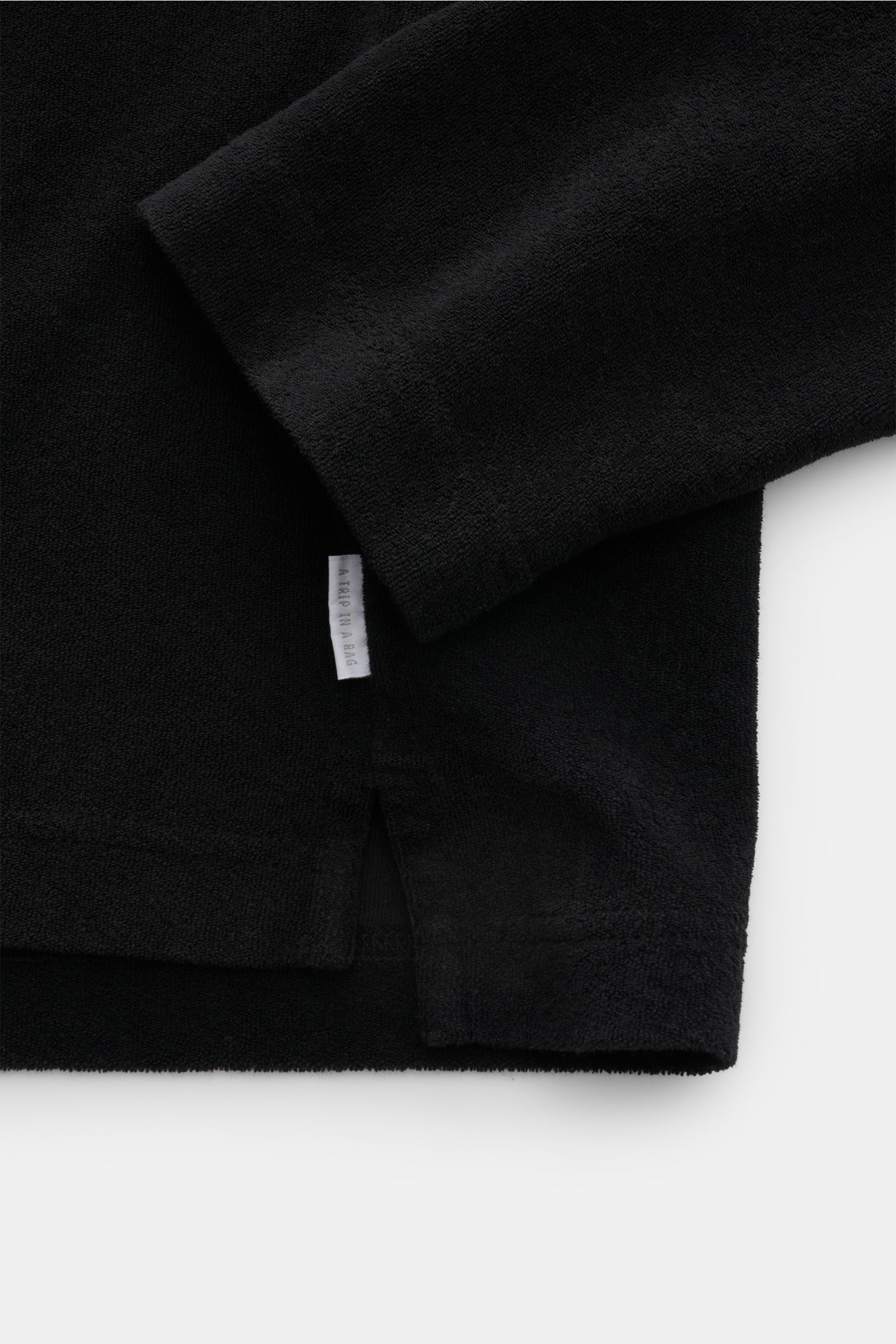 Close-up detail shot of the sleeve and side seam of the 04651/ A trip in a bag Terry hooded jumper 'Terry' black, showing the soft pure cotton terrycloth fabric and small woven label. Comfort and coolness with summery nonchalance: The hooded jumper 'Te