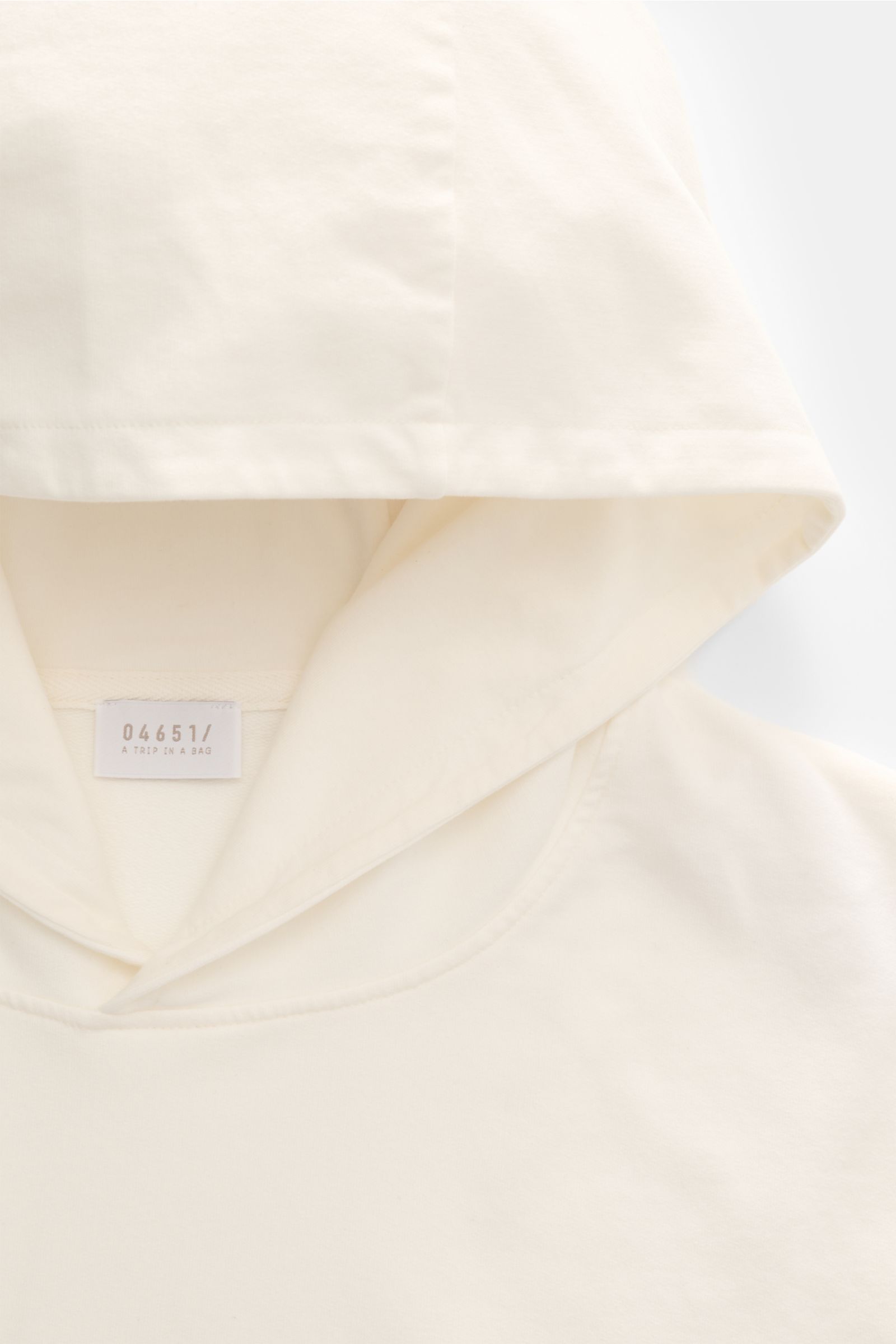 04651/ A trip in a bag Kapuzenpullover 'IF Hoodie' creme, Detailansicht der Kapuze aus gebürstetem Jersey mit weichem Griff und kleinem Weblabel, von oben fotografiert.