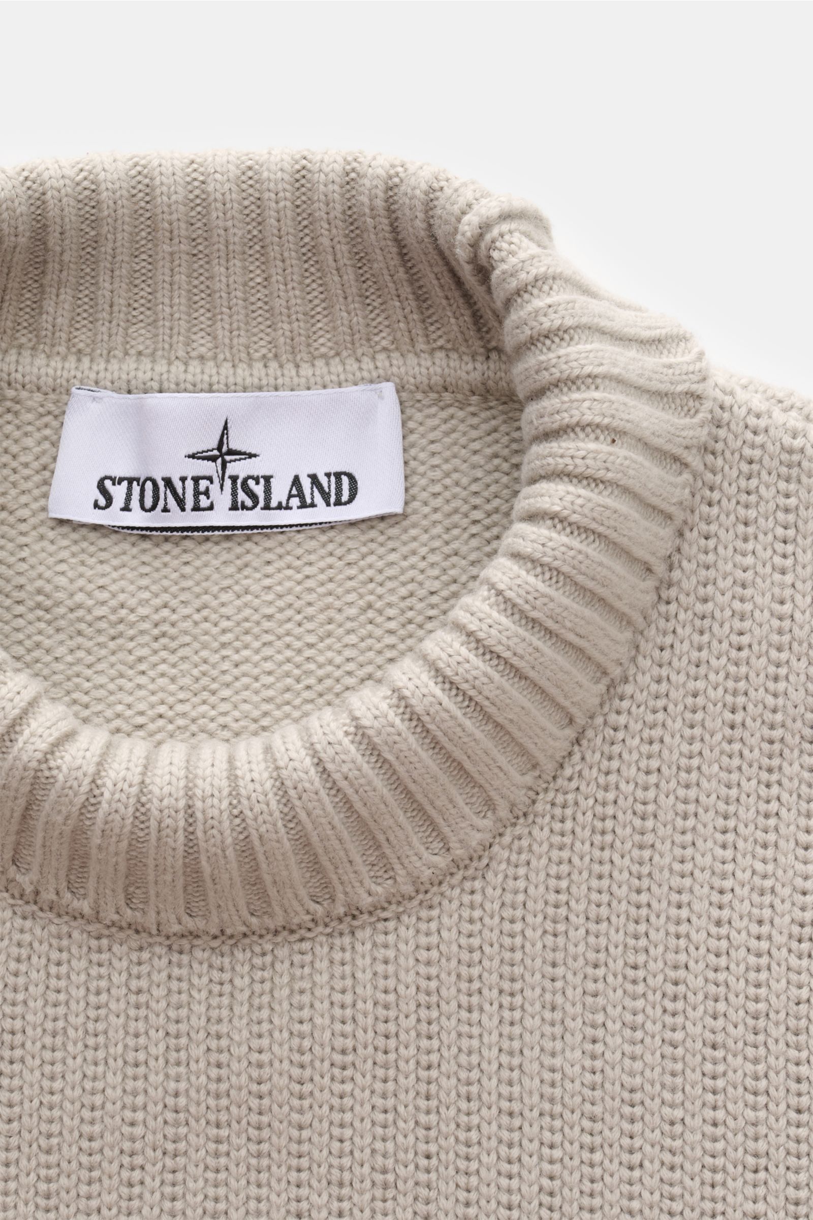 Nahaufnahme des Stone Island Pullovers hellgrau aus dichtem Baumwoll-Microfaser-Strick mit Stehkragen und Kompass-Badge am Oberarm, von oben fotografiert.