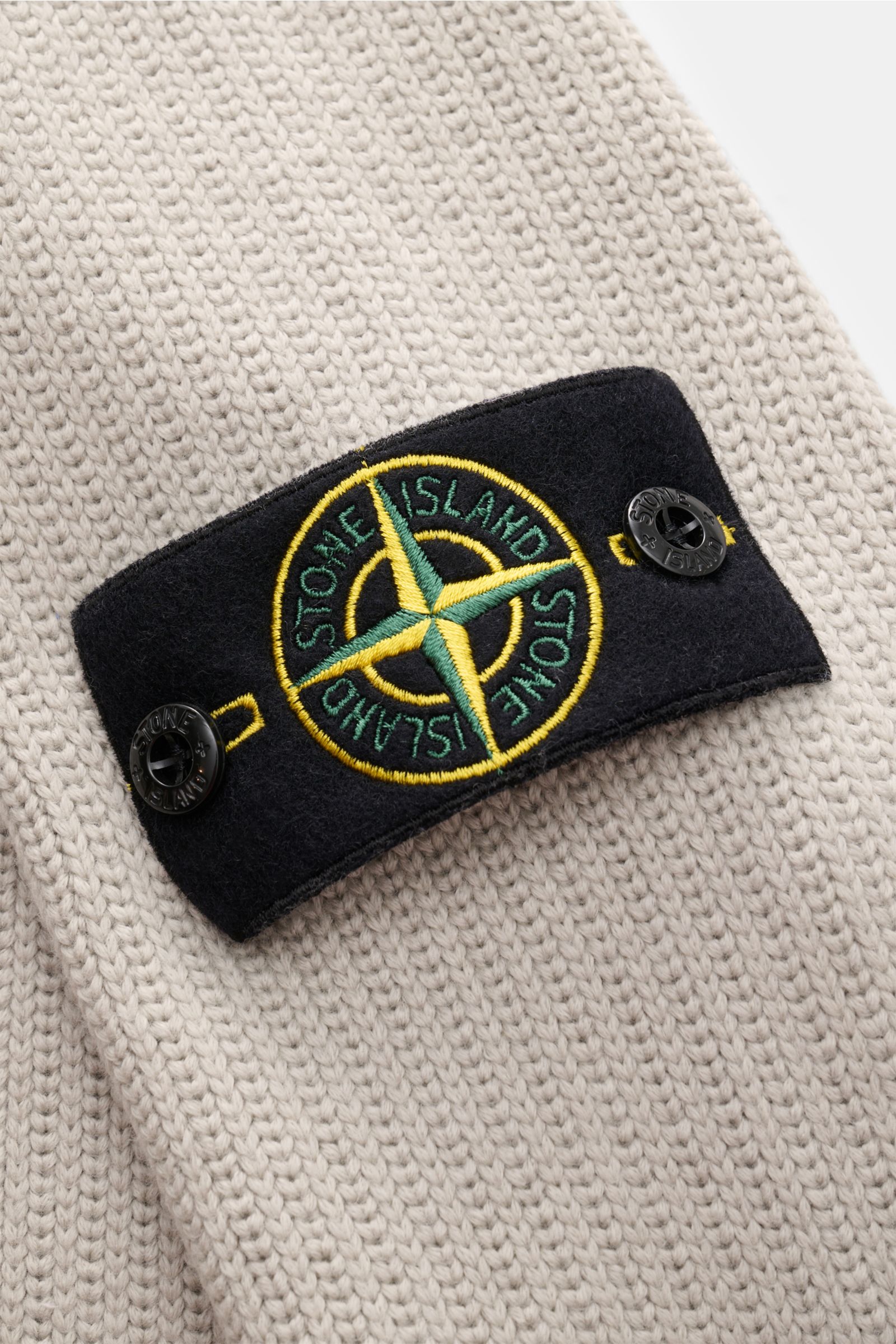 Stone Island Pullover hellgrau aus Baumwoll-Microfaser-Strick, Detailaufnahme von oben zeigt das Kompass-Badge am Ärmel, Slim Fit mit Stehkragen und Rippbündchen.