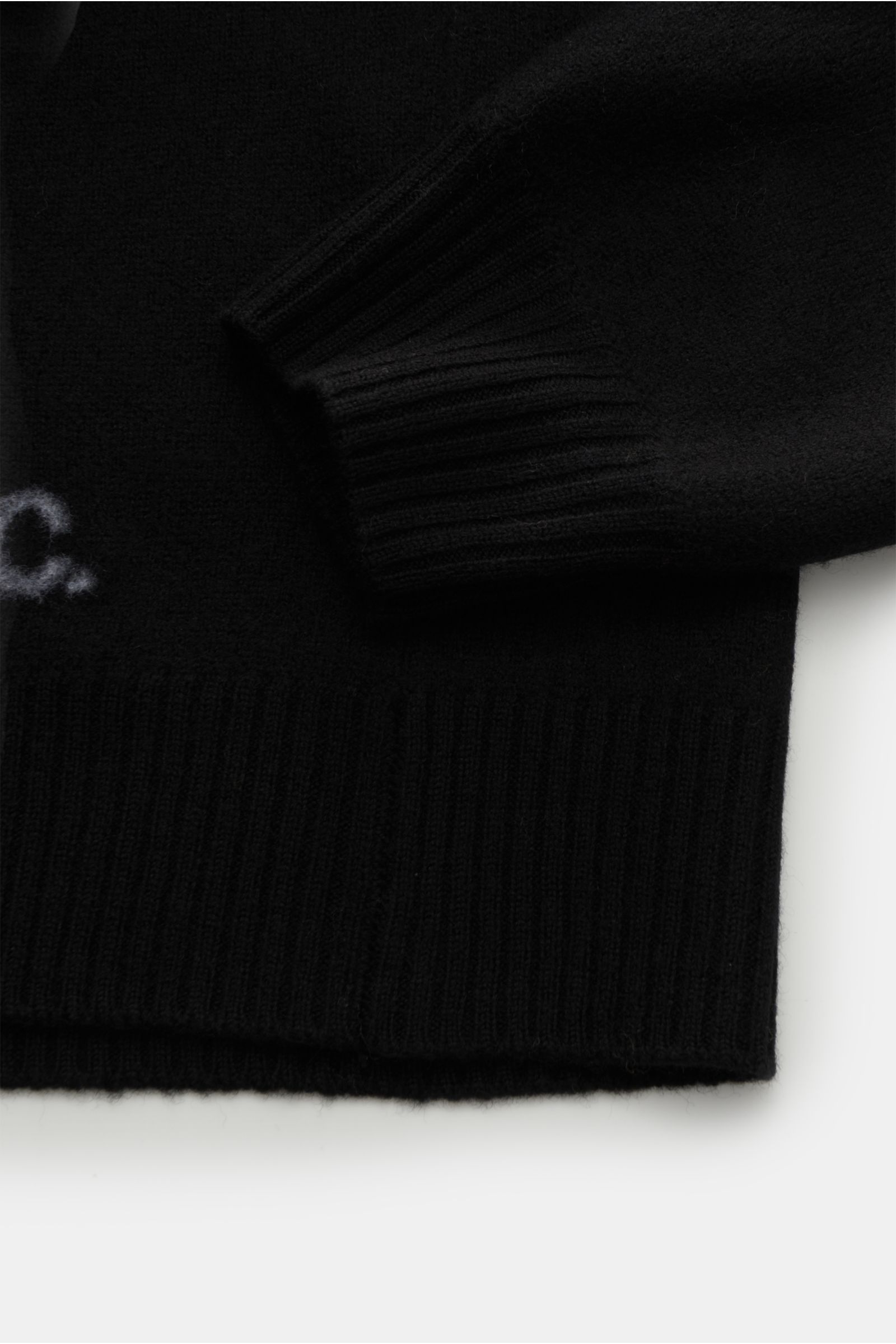 Close-up image of the lower section and sleeve cuff of the A.P.C. Rollkragenpullover 'Walter' schwarz, photographed from above, showing reine Wolle, weicher Griff, mittelfeines Strickbild, Regular Fit, anliegender Rollkragen aus Rippstrick, flexible Rippb