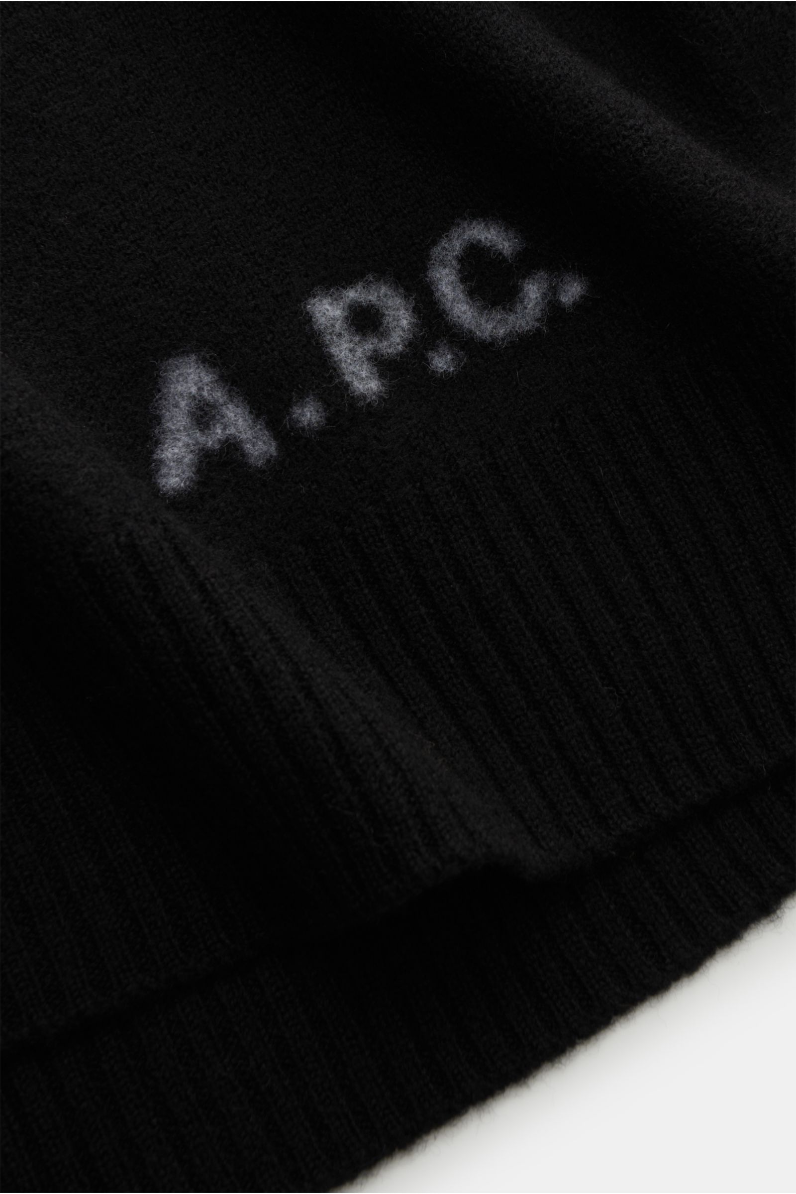 Close-up view of the A.P.C. Rollkragenpullover 'Walter' schwarz showing the soft black wool fabric with a subtle A.P.C. logo on the front, featuring reine Wolle, weicher Griff, mittelfeines Strickbild, Regular Fit, anliegender Rollkragen aus Rippstrick, f