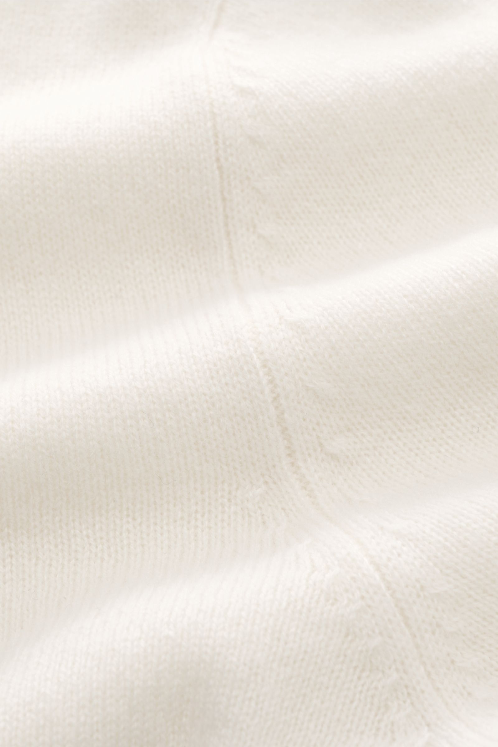 Nahaufnahme des feinen Strickbilds und der weichen Haptik des FTC Cashmere Rollkragenpullovers offwhite mit Rippbündchen.