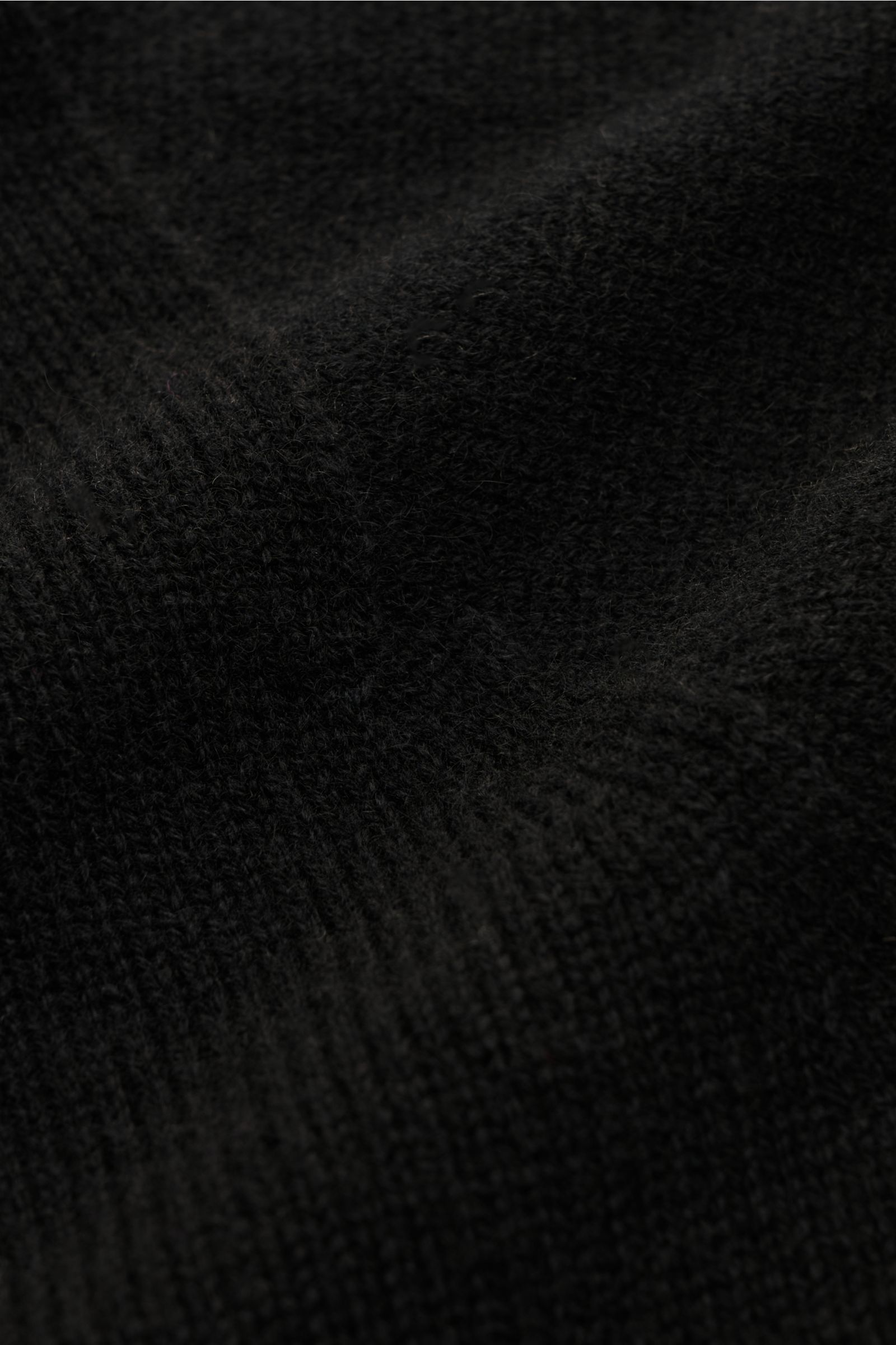 Nahaufnahme aus schräger Perspektive des schwarzen 04651/ A trip in a bag Cashmere Rollkragenpullovers mit feinem Strickbild und Rippbündchen.