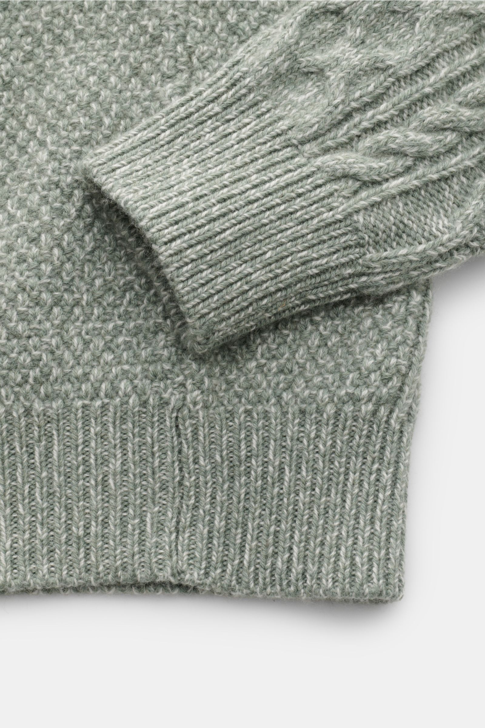 Nahe Aufnahme des 04651/ A trip in a bag Rollkragenpullover 'Mouline Cable Turtle' graugrün meliert mit grobem Zopfstrickmuster, Rippbündchen und Woll-Cashmere-Bouclé aus der Vogelperspektive.