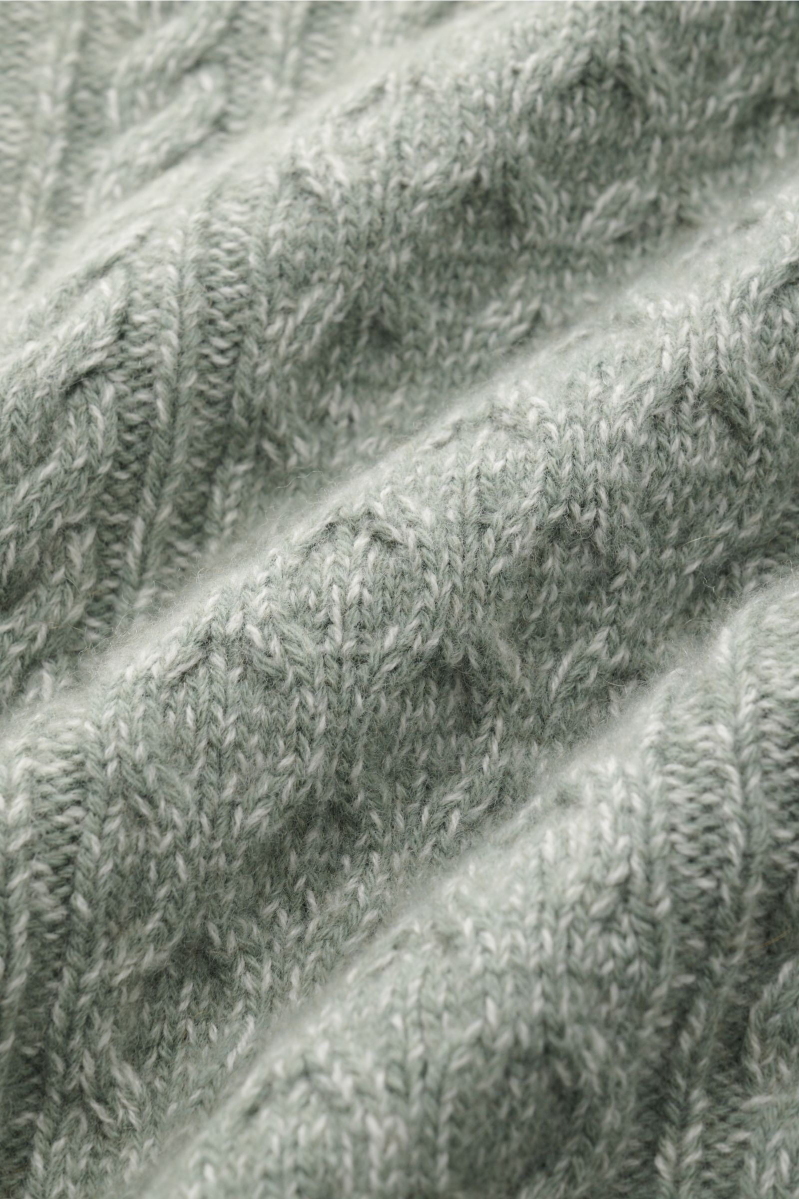 Nahaufnahme des grob gestrickten Zopfstrickmusters des 04651/ A trip in a bag Rollkragenpullovers 'Mouline Cable Turtle' graugrün meliert aus Wolle-Cashmere-Bouclé, weich und voluminös.