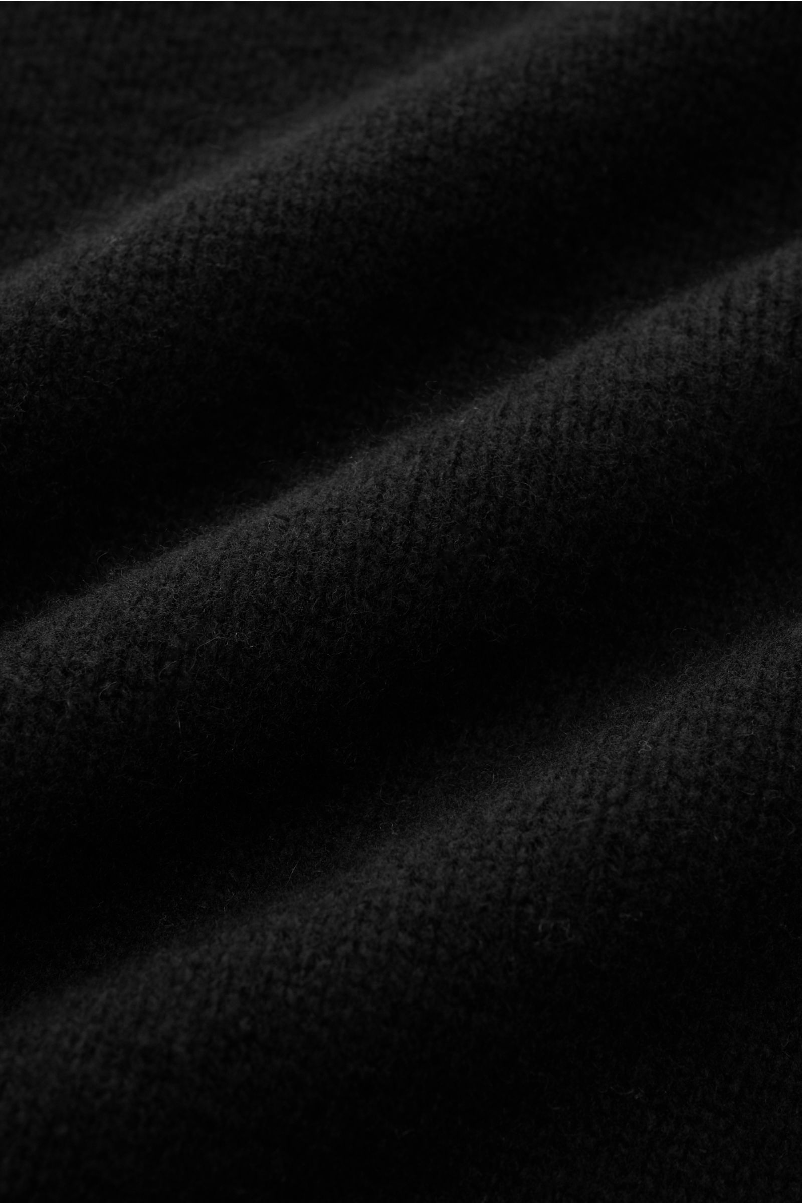 Close-up image of the fabric texture of the 04651/ A trip in a bag Kapuzenpullover schwarz, showing a soft mix of wool and cashmere with a mittelfeines Strickbild, photographed from a top-down perspective. Features include a softer feel, Regular Fit, hohe