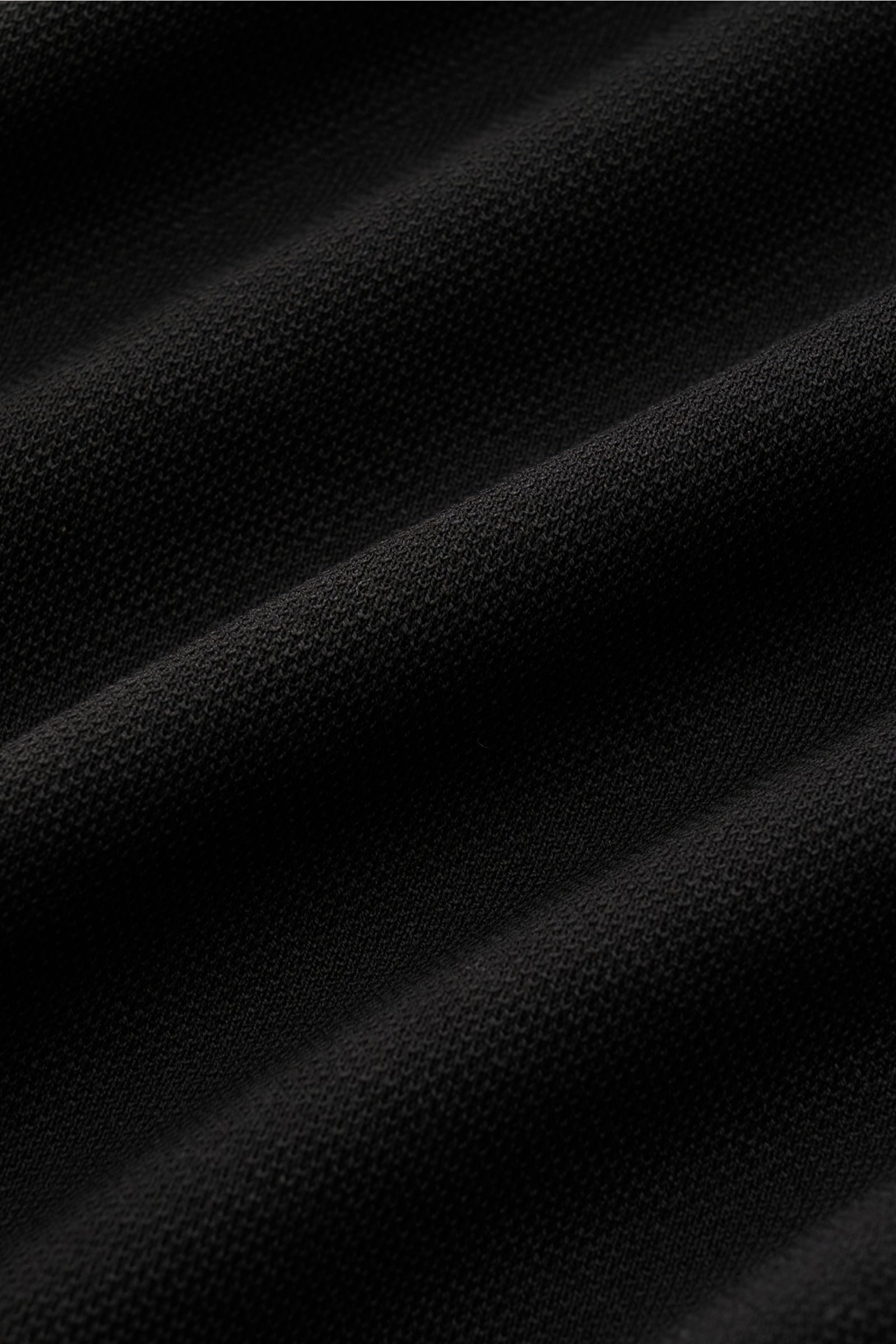 Close-up texture view of the black 04651/ A trip in a bag Rollkragenpullover 'Tp Turtle' schwarz showing fine cotton piqué knit from a diagonal perspective.

Vielseitiges Essential: Mit seinem zeitlosen Design wird der Rollkragenpullover von 04651/ A T