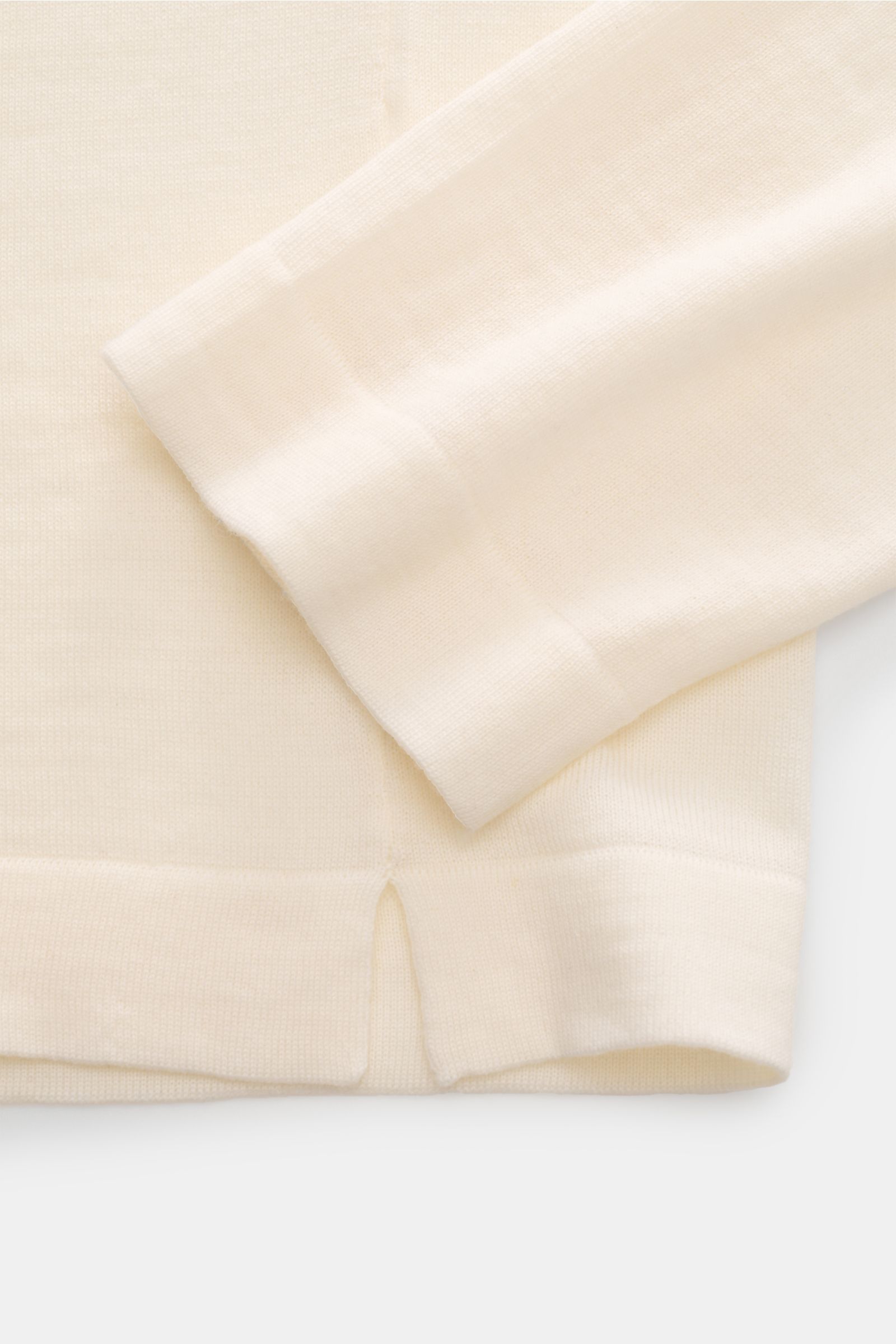 Close-up view of the sleeve and hem with short side slit of the 04651/ A trip in a bag Merino Rollkragenpullover creme, made from pure merino wool with soft touch, fine knit, slim fit, ribbed turtleneck, and short hem slits.