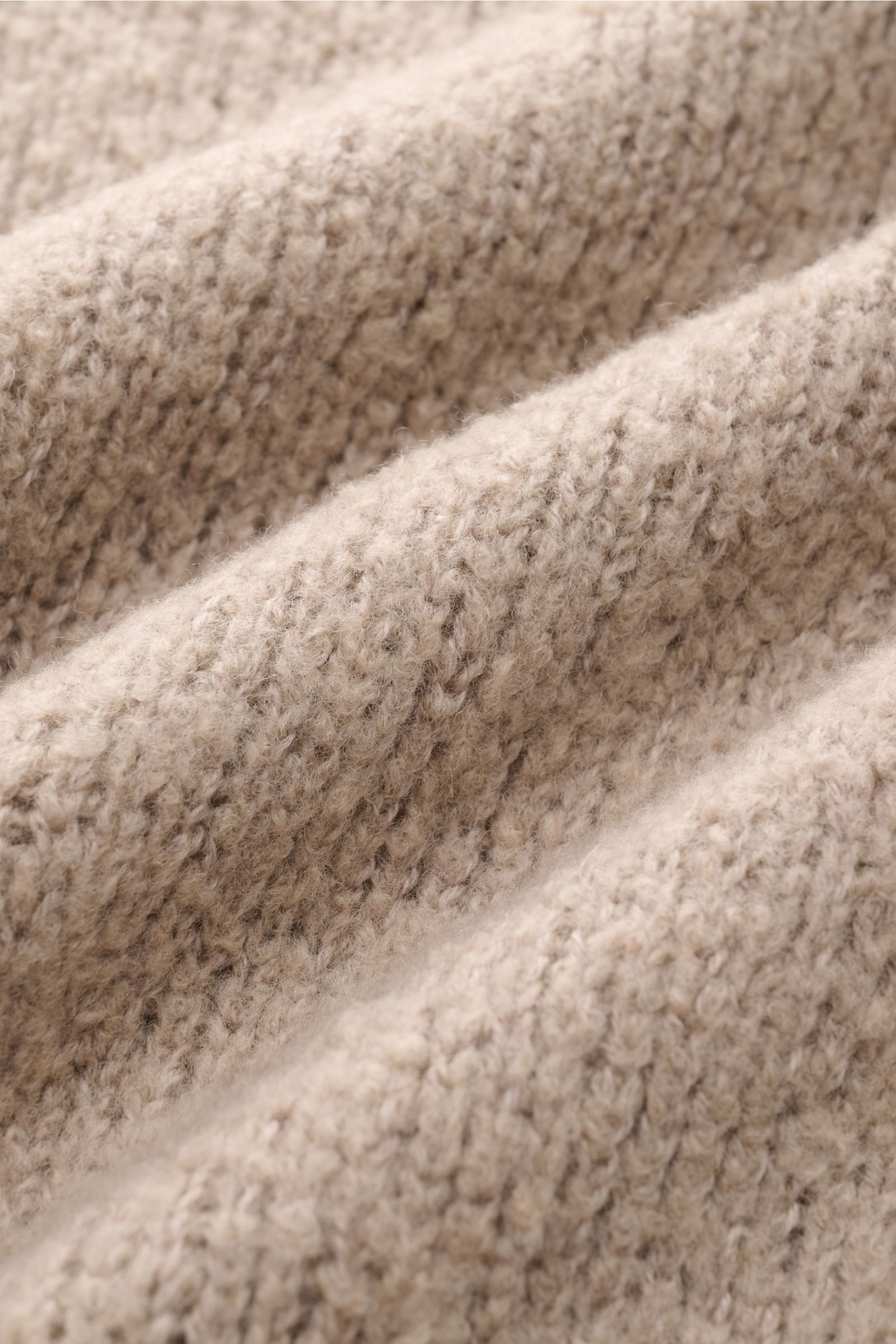 Close-up view of the beige knit texture of the 04651/ A trip in a bag Rollkragenpullover 'Chunky Turtle' showing soft, voluminous wool fibers. Edles Winter-Essential: Der legere 'Chunky Turtle' Rollkragenpullover von 04651/ A TRIP IN A BAG wird mit sei
