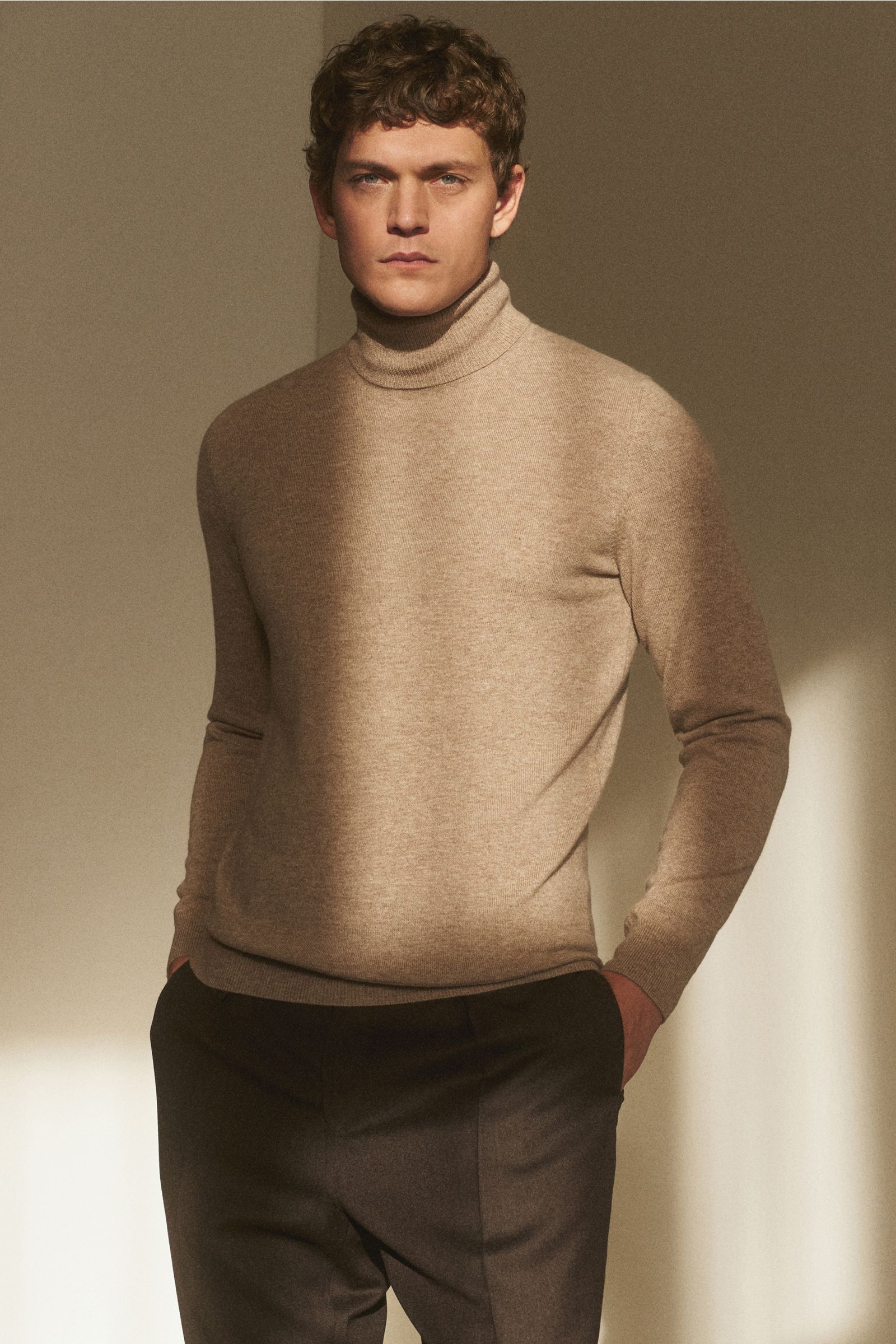 Mann frontal stehend, trägt von Braun Cashmere Rollkragenpullover beige, Slim Fit, fein gestrickt, weicher Griff, anliegender Rollkragen, elastische Rippbündchen.