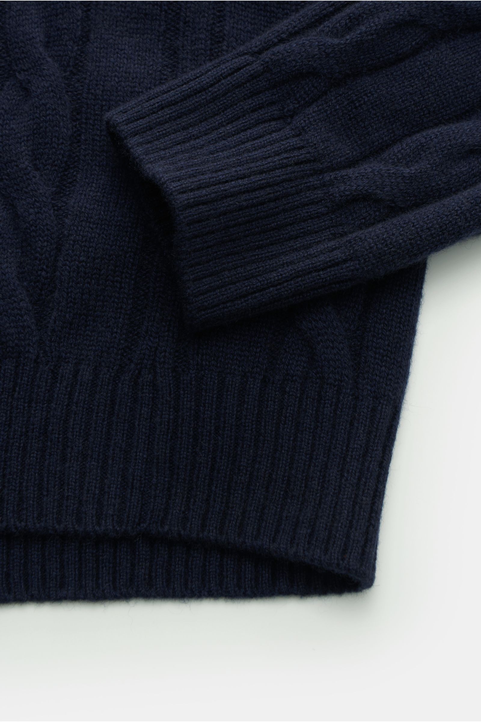Nahaufnahme von Ärmel und Bund des von Braun Cashmere Rollkragenpullover navy mit klassischem Zopfstrickmuster, weichem Griff, Regular Fit, anliegendem Rollkragen und flexiblen Rippbündchen.