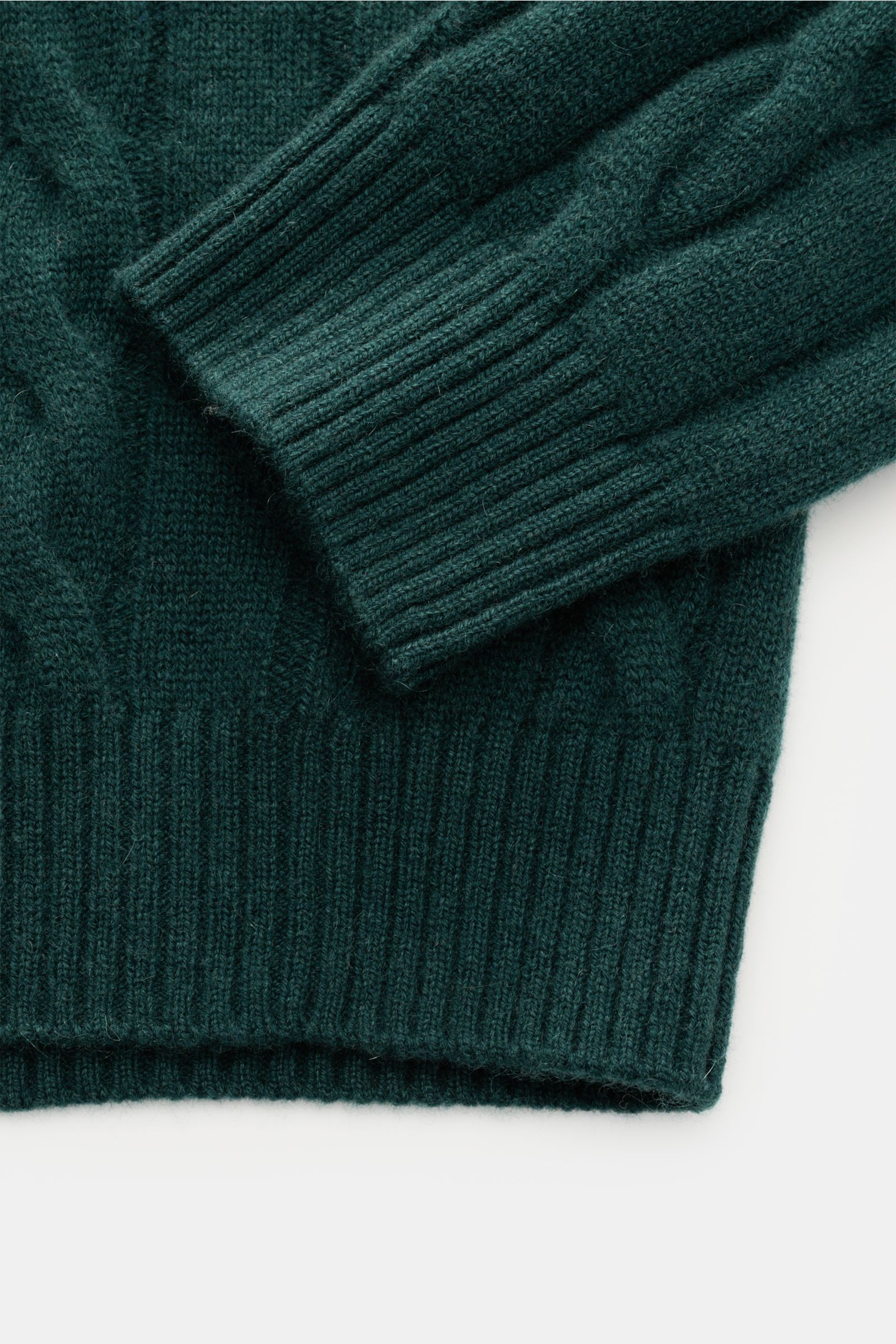 Nahaufnahme von Bündchen und Ärmel des von Braun Cashmere Rollkragenpullovers dunkelgrün mit klassischem Zopfstrickmuster, Regular Fit und flexiblem Rippbündchen, gefertigt aus weichem, reinem Cashmere aus der inneren Mongolei.